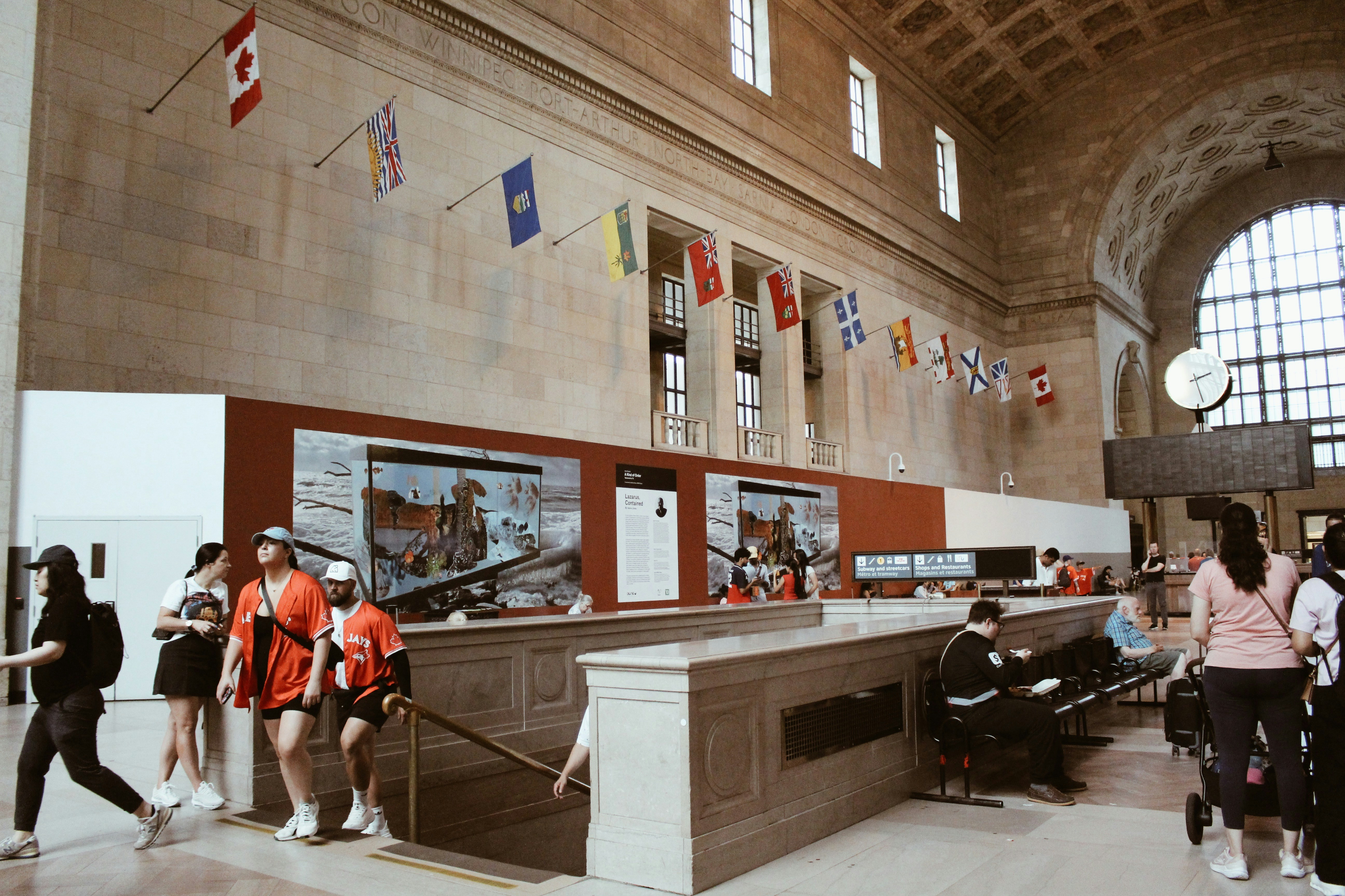 People walking in a grand hall with flags and displays.