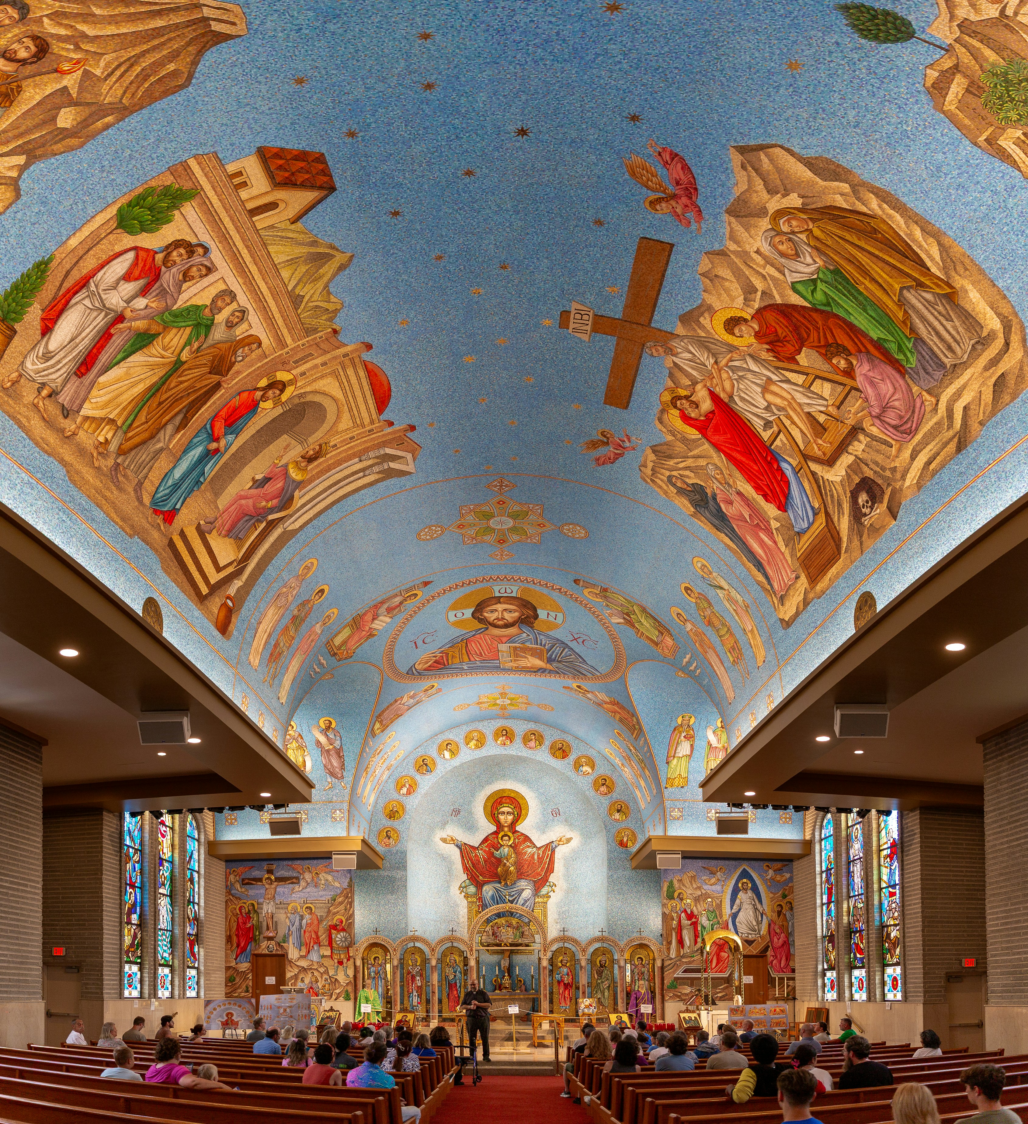 Interno della chiesa ornato con murales religiosi, mosaici e congregazioni con posti a sedere.