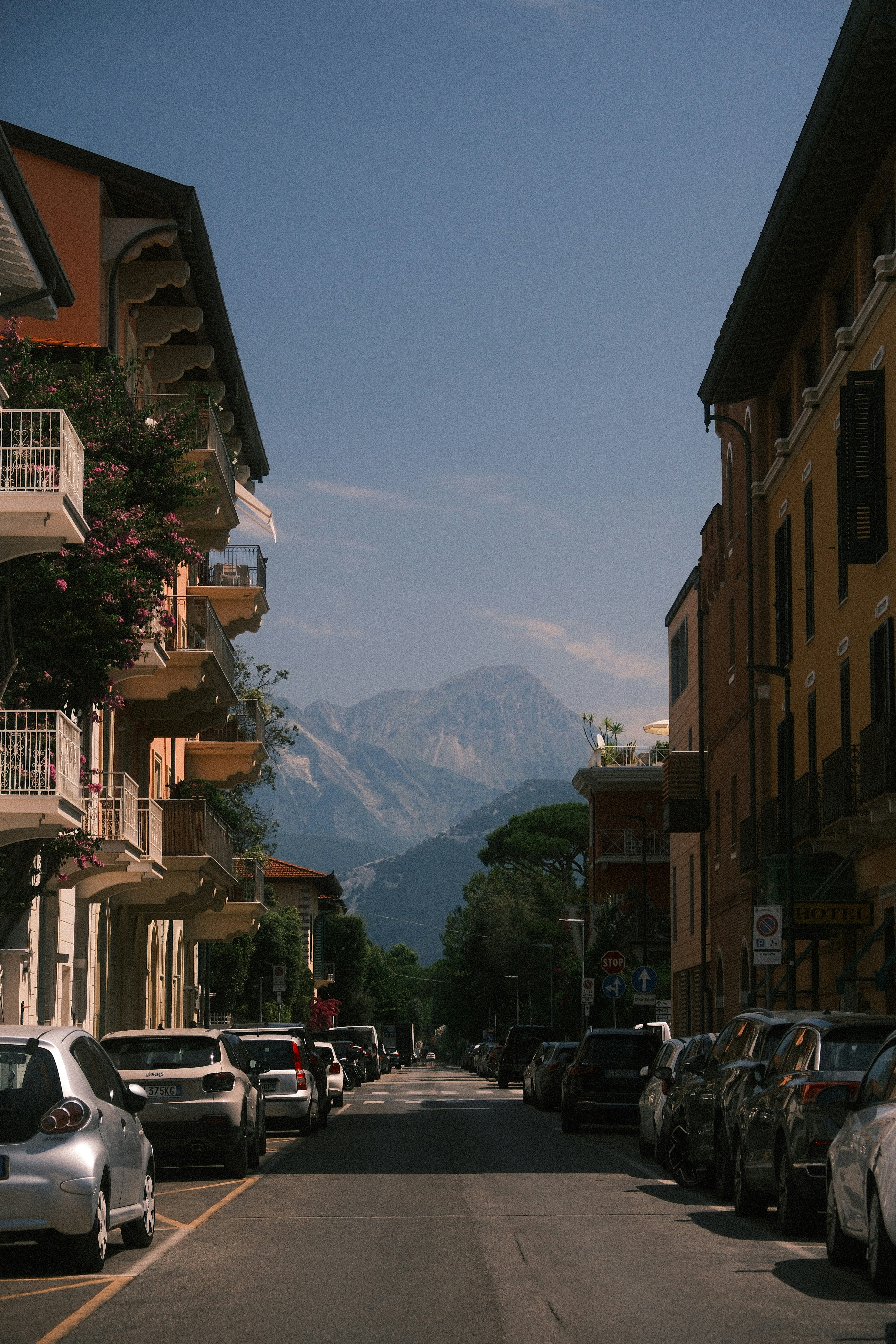 A street with parked cars and buildings leading to mountains