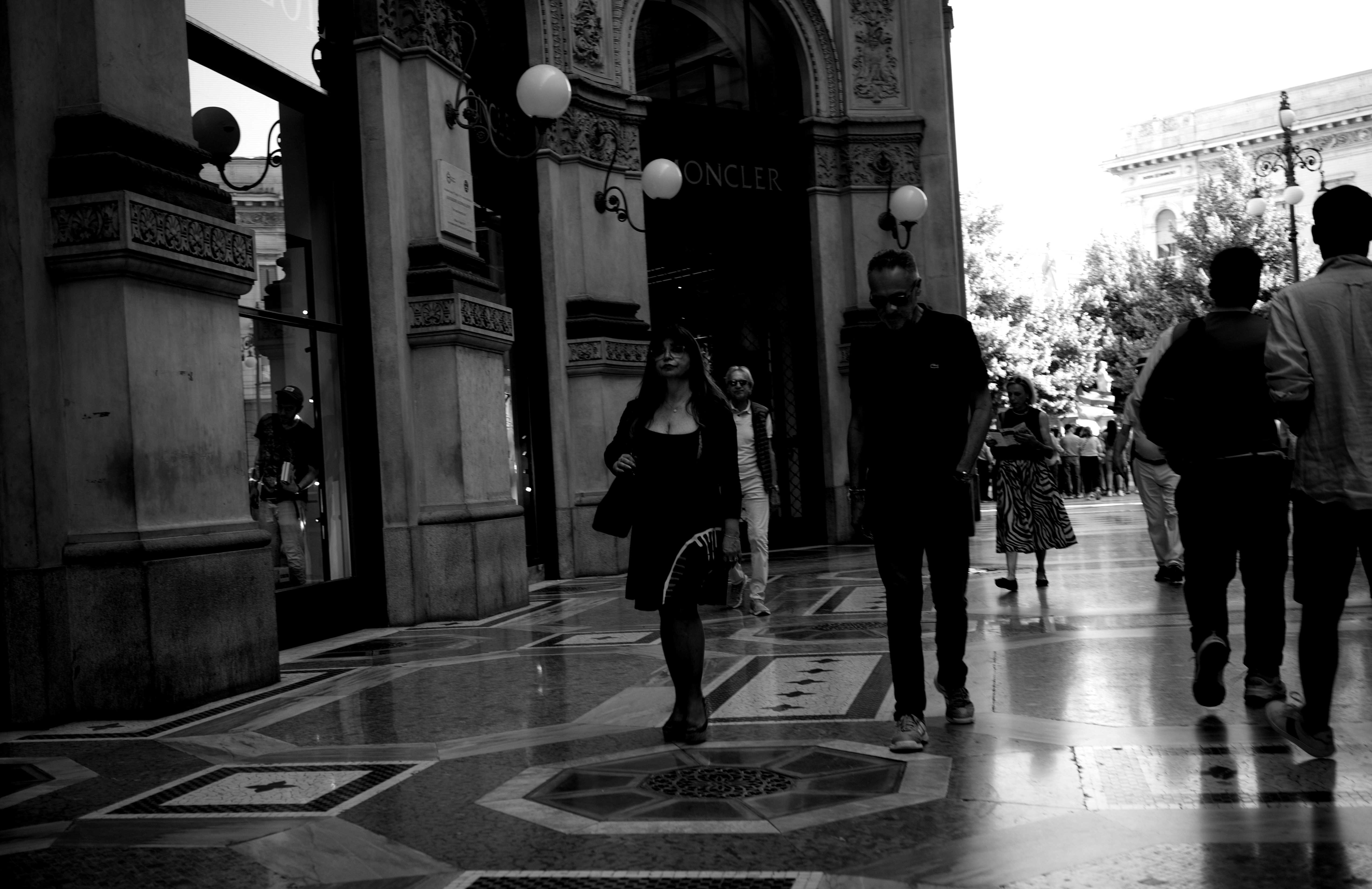 People walk on a patterned floor near a grand building.