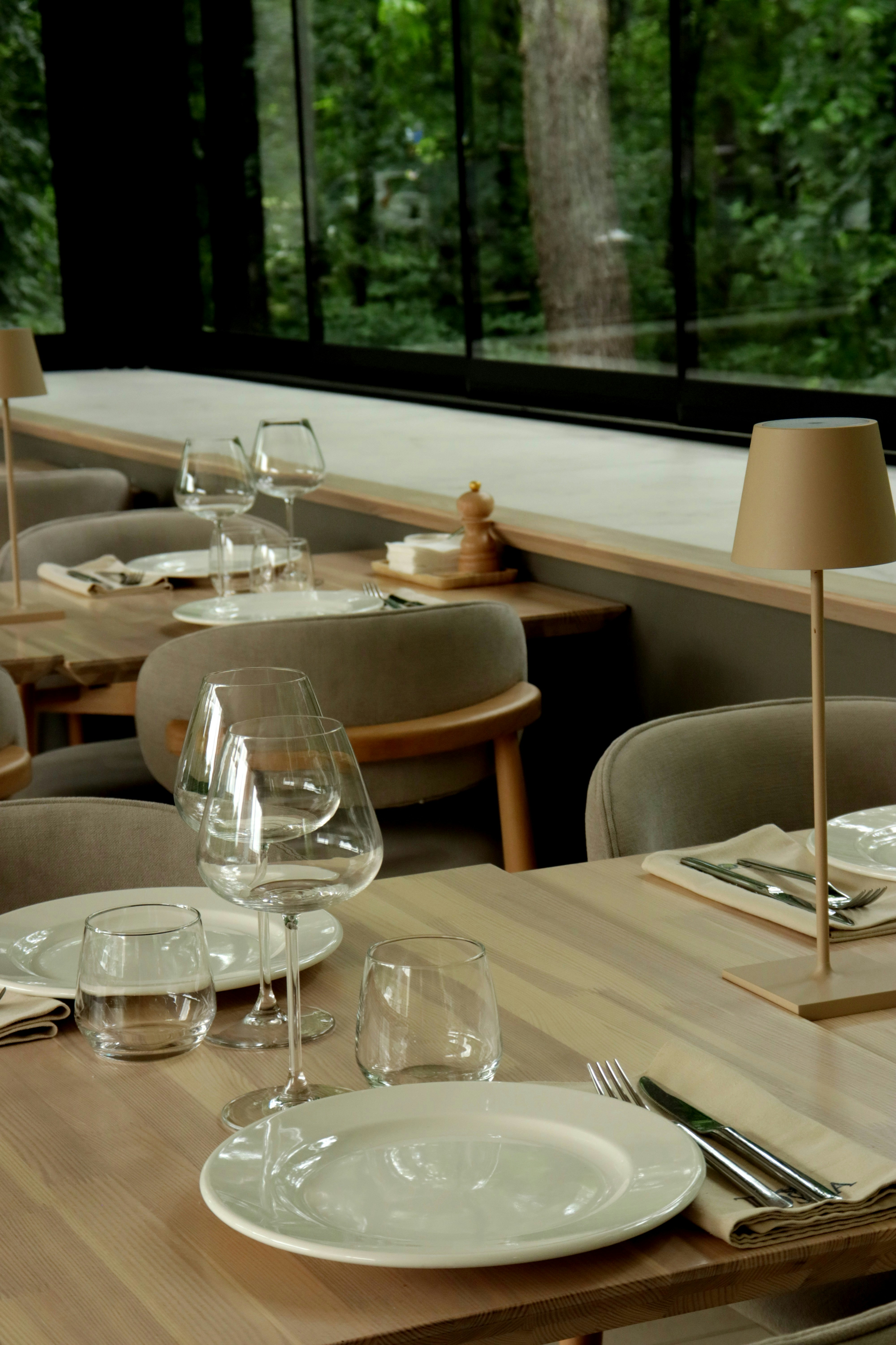 Mesas de comedor del restaurante con platos, copas y vistas al bosque.