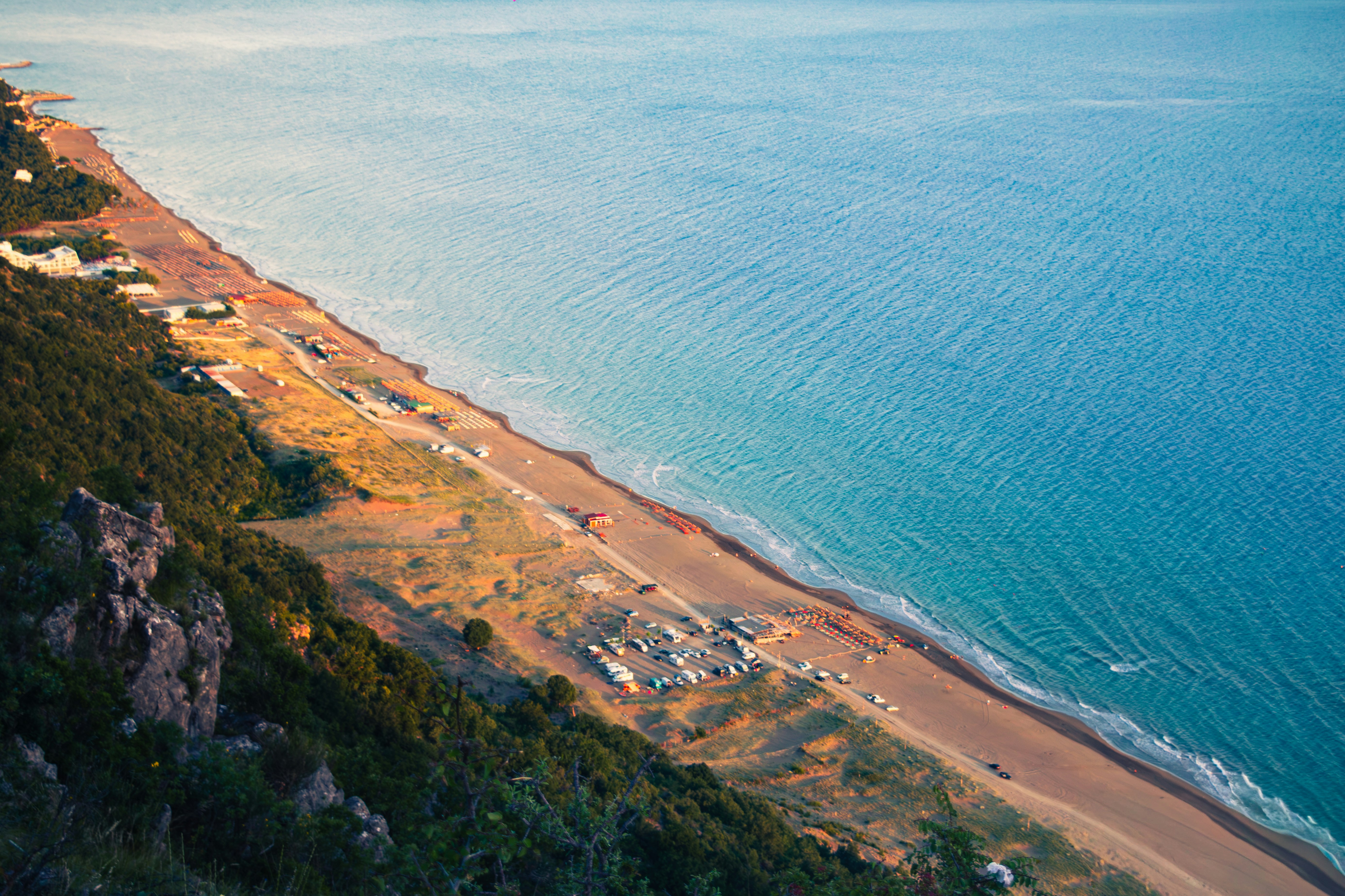 Coastal landscape with sandy beach, blue ocean, and green hillside.