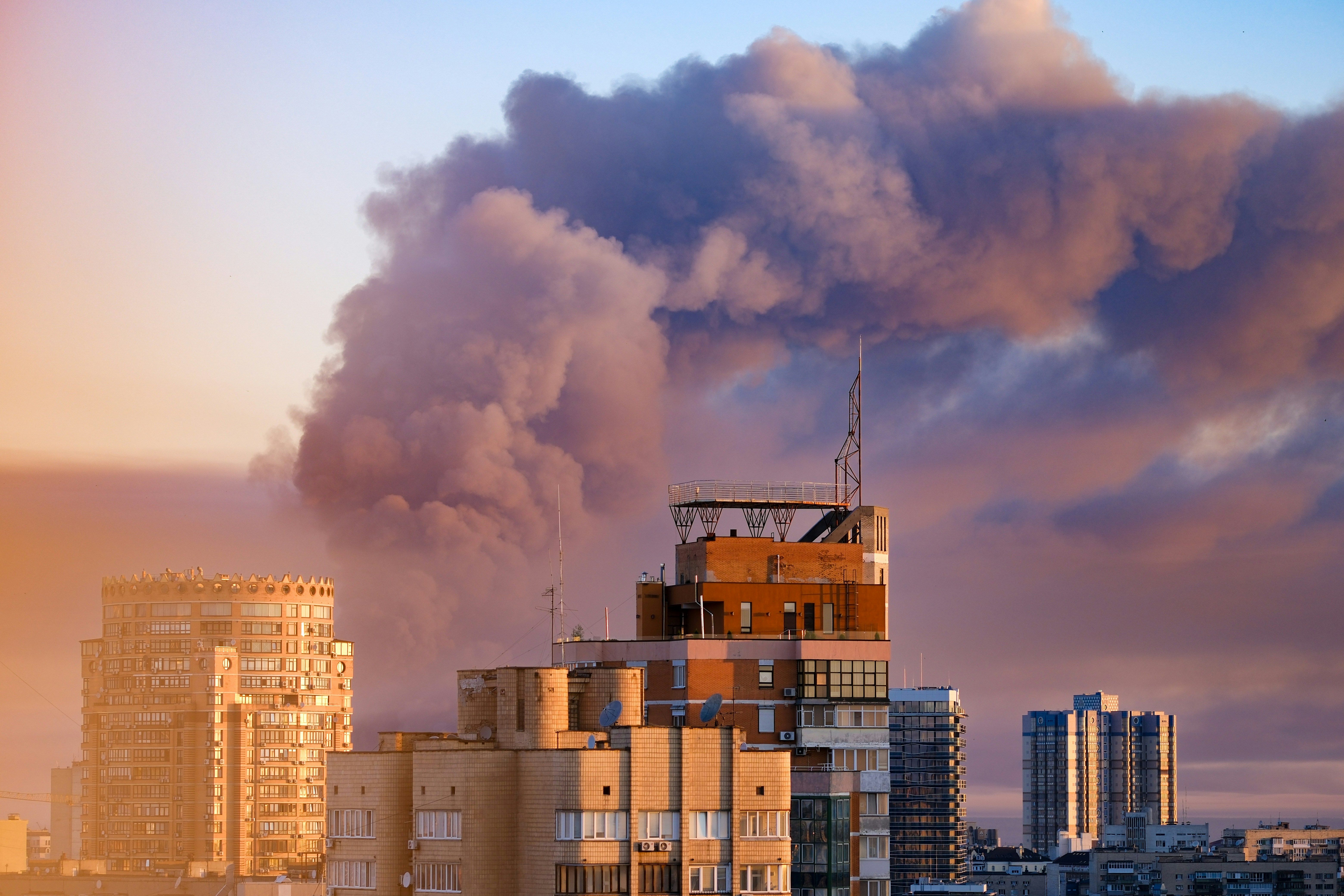Thick smoke plume above city buildings at sunset