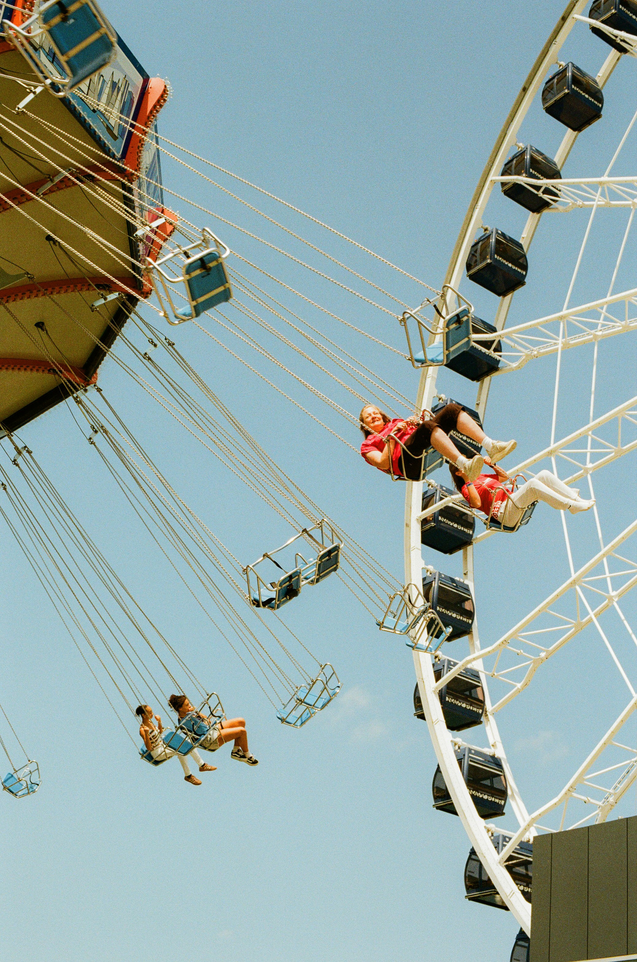 People enjoying swing ride and ferris wheel under blue sky.