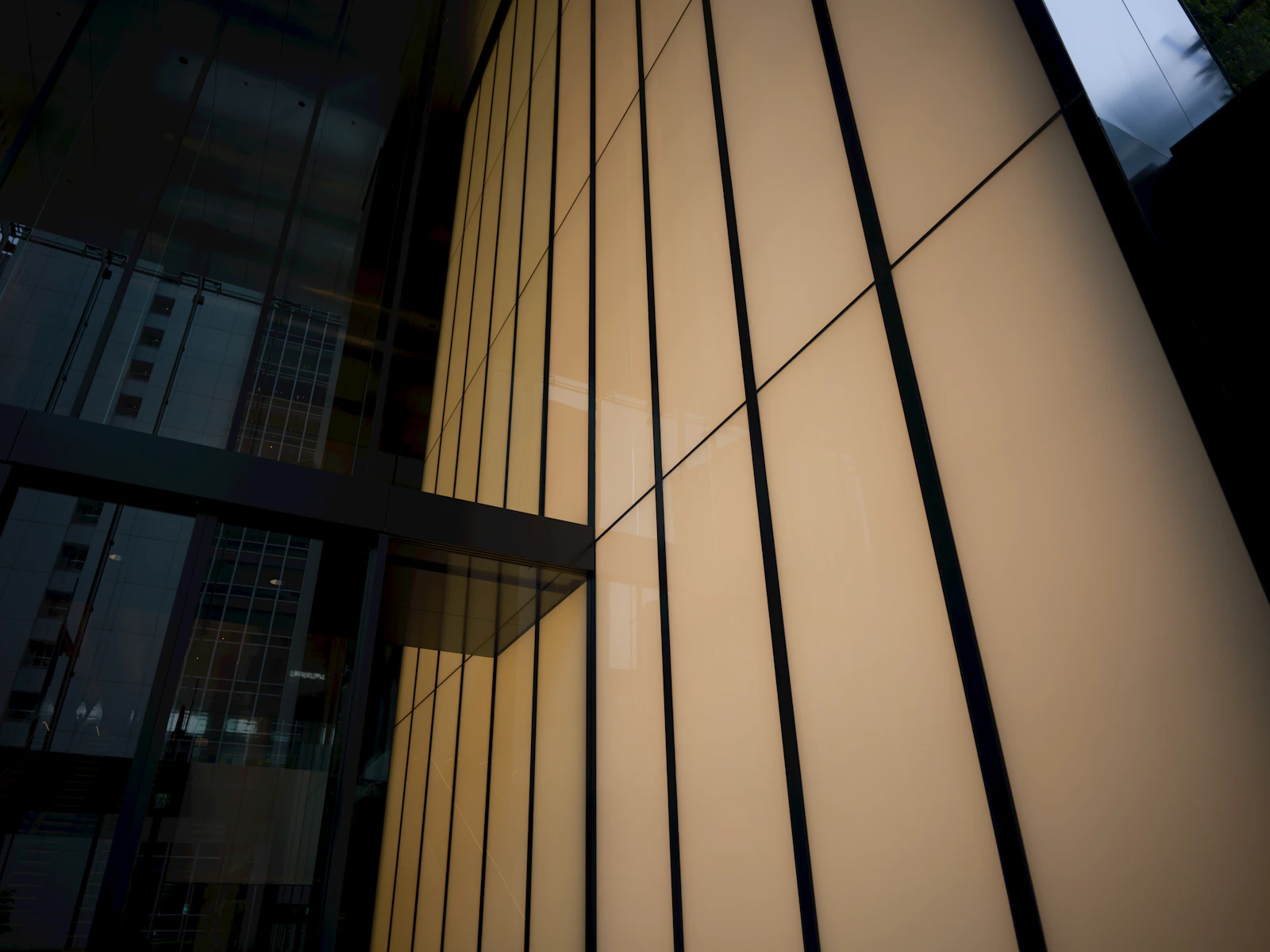 Dark glass building facade at dusk with vertical panels glowing warm gold