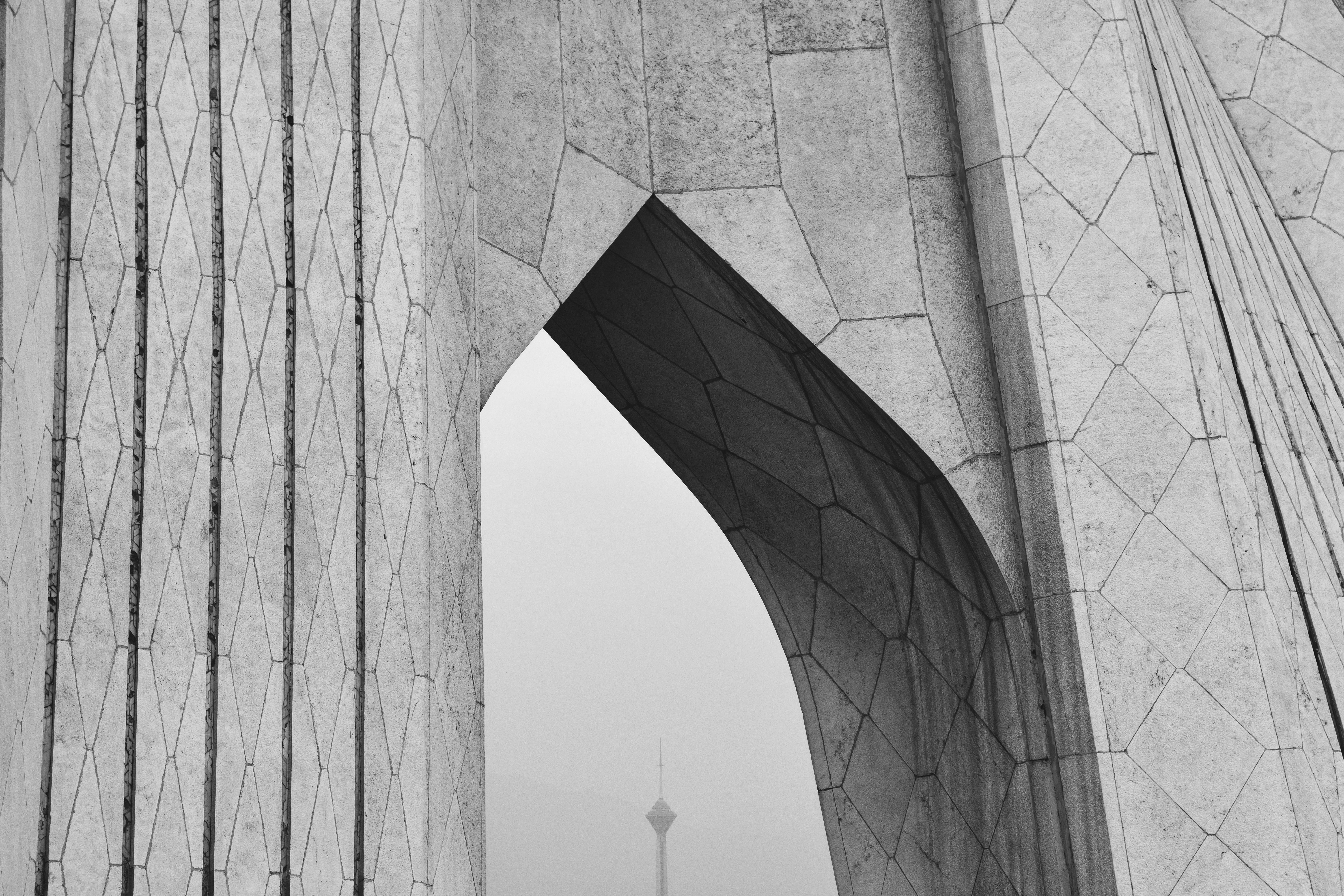 Une arche géométrique encadre une tour lointaine en noir et blanc.