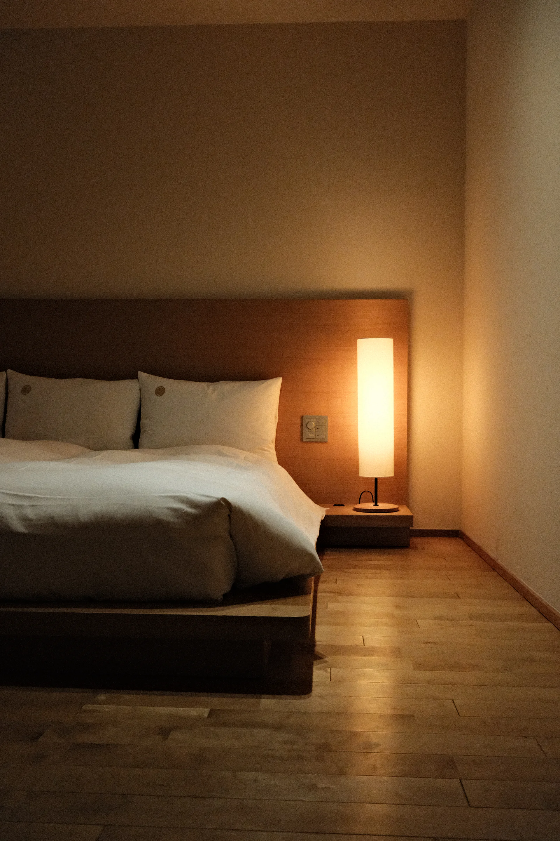 Minimal bedroom with a low wooden bed, white linen and a warm lamp