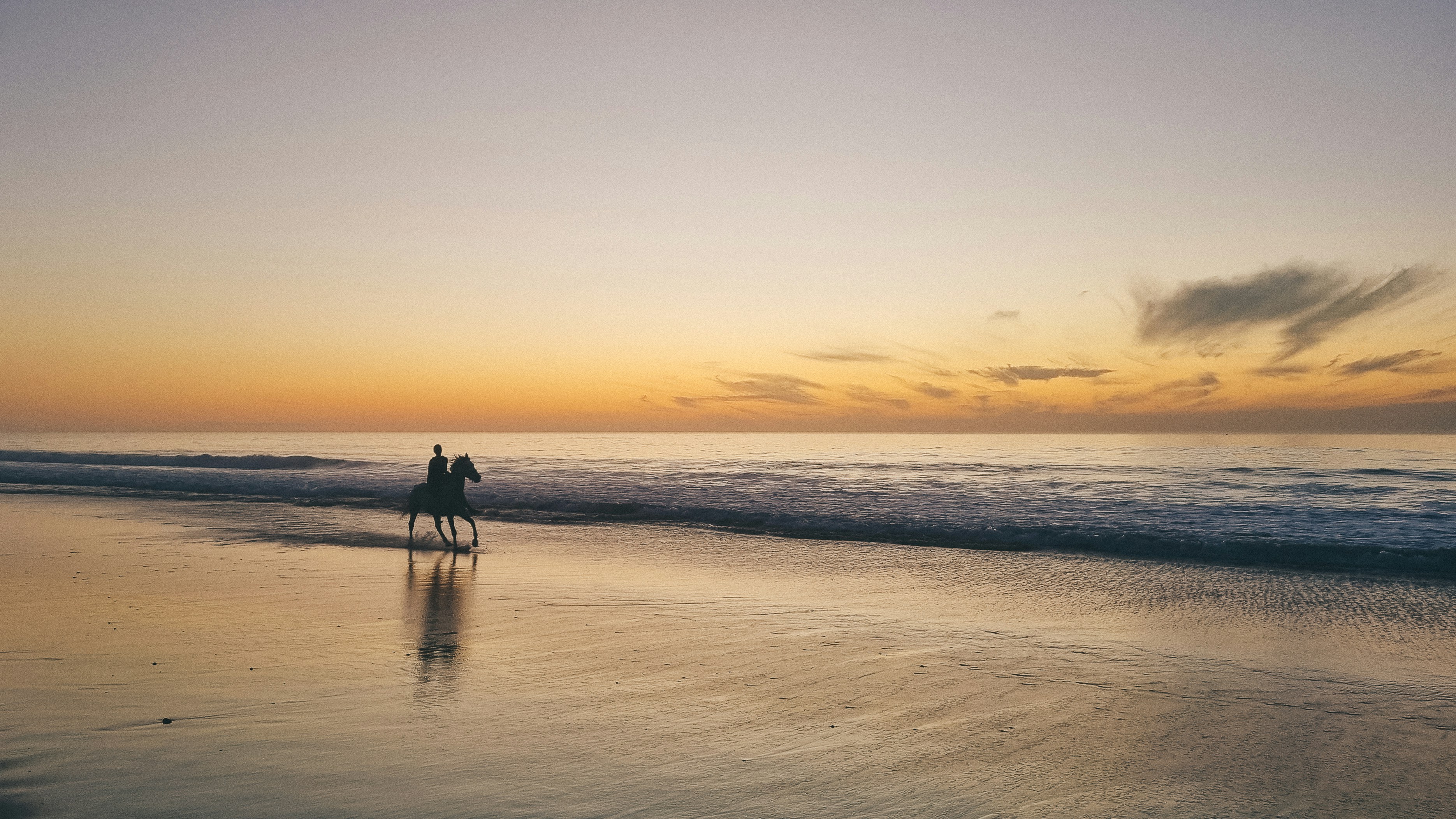 A person riding a horse on a beach at sunset.
