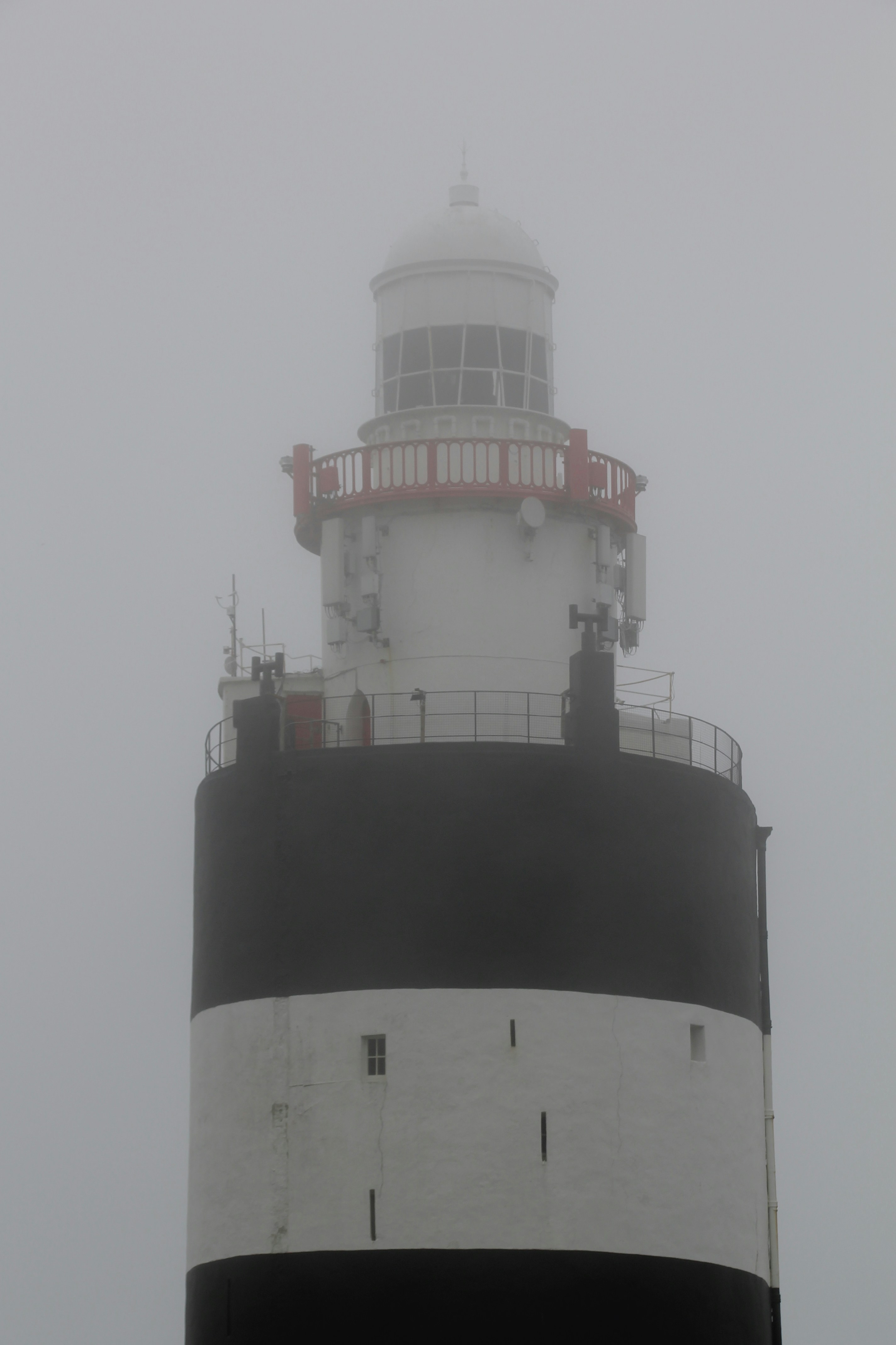 Un alto faro bianco e nero avvolto da una fitta nebbia.