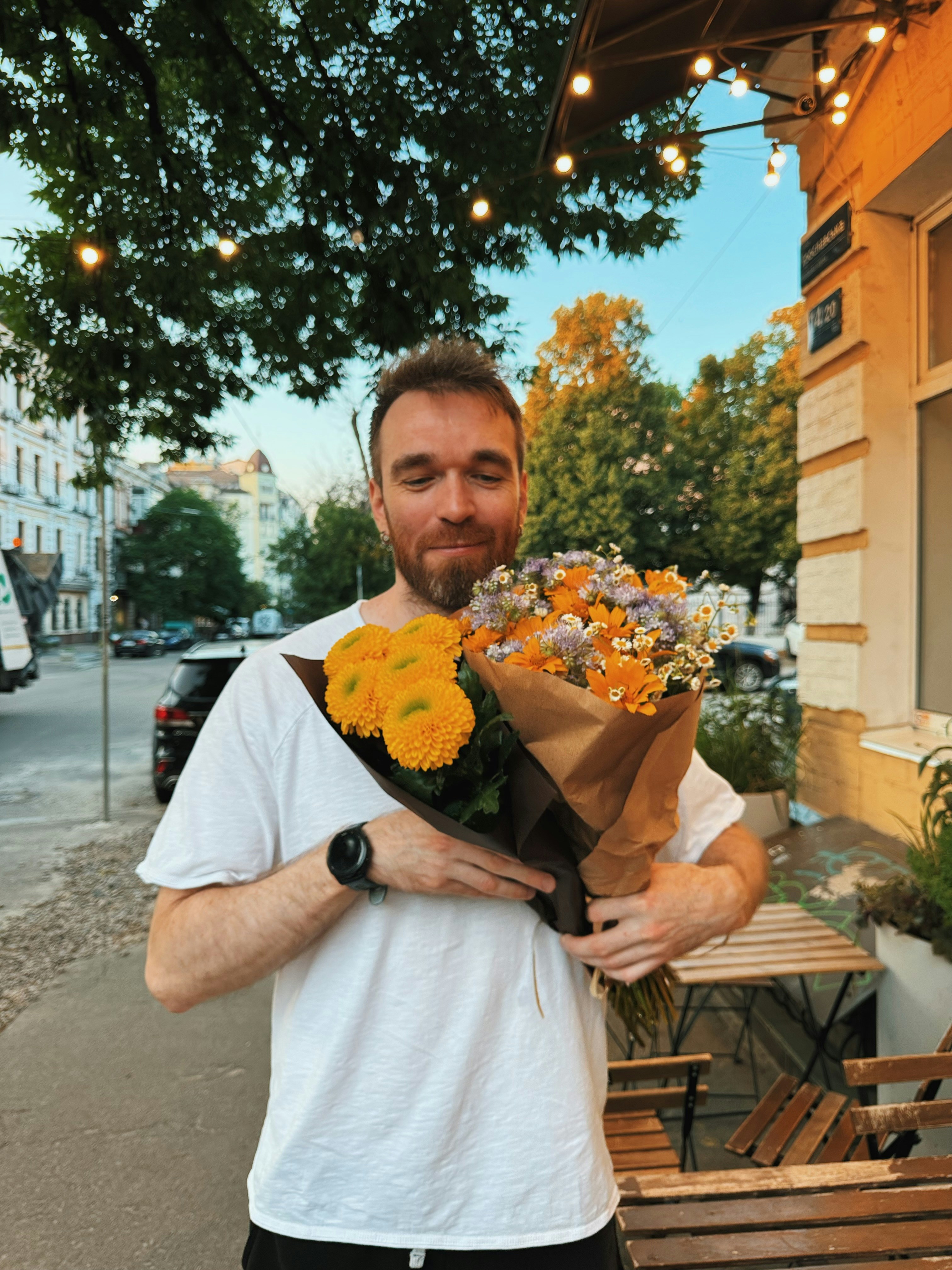A man holding two bouquets of colorful flowers outdoors.