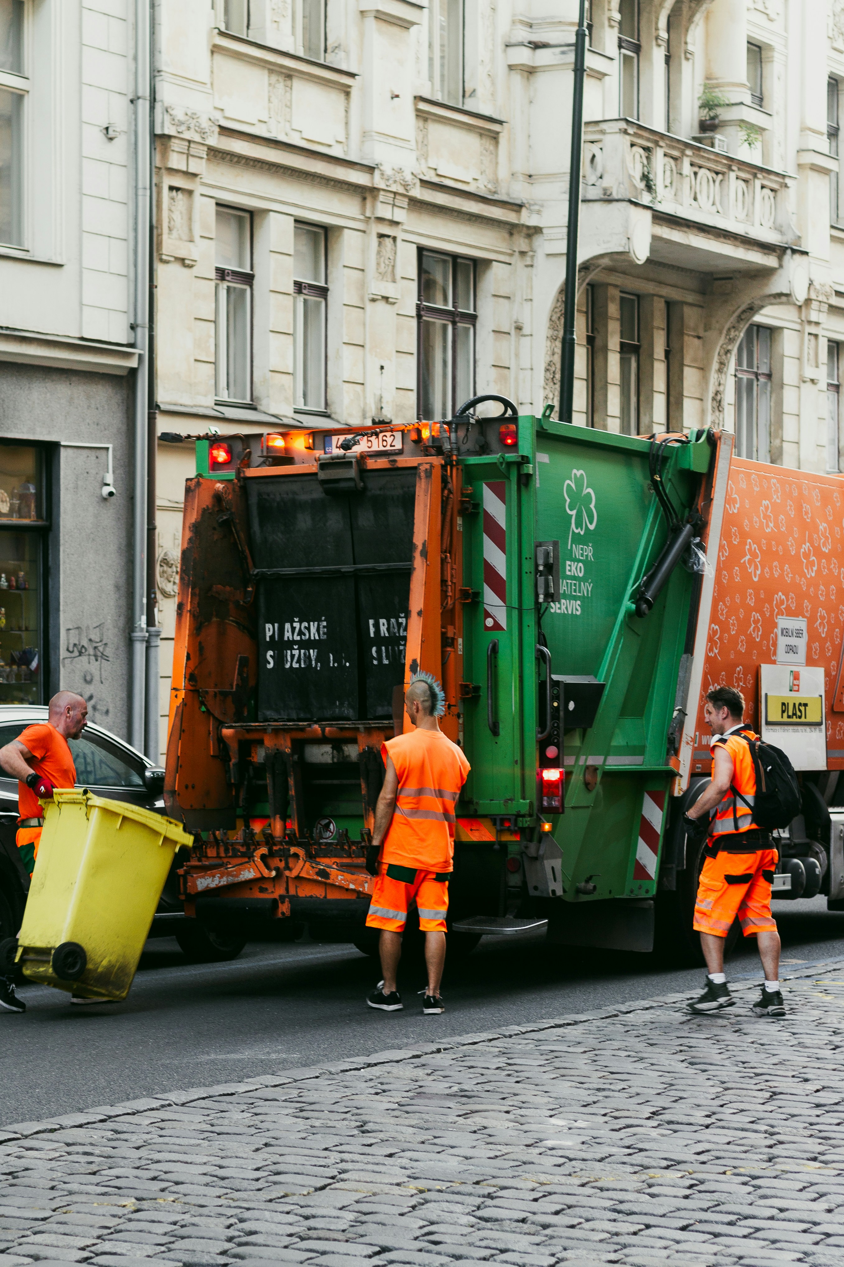 Sanitation workers loading a yellow bin into a garbage truck.