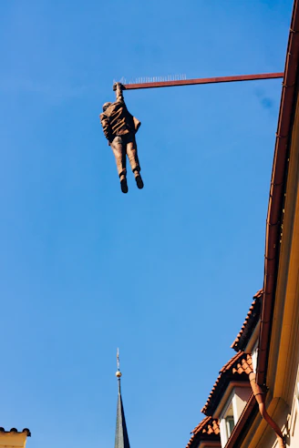 Man sculpture hangs from beam against blue sky