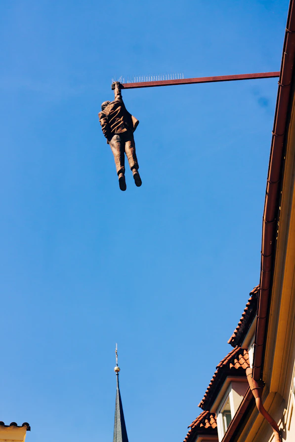 Man sculpture hangs from beam against blue sky