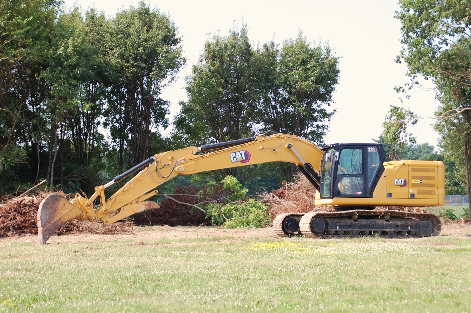 A tracked excavator clearing brush along the edge of a property