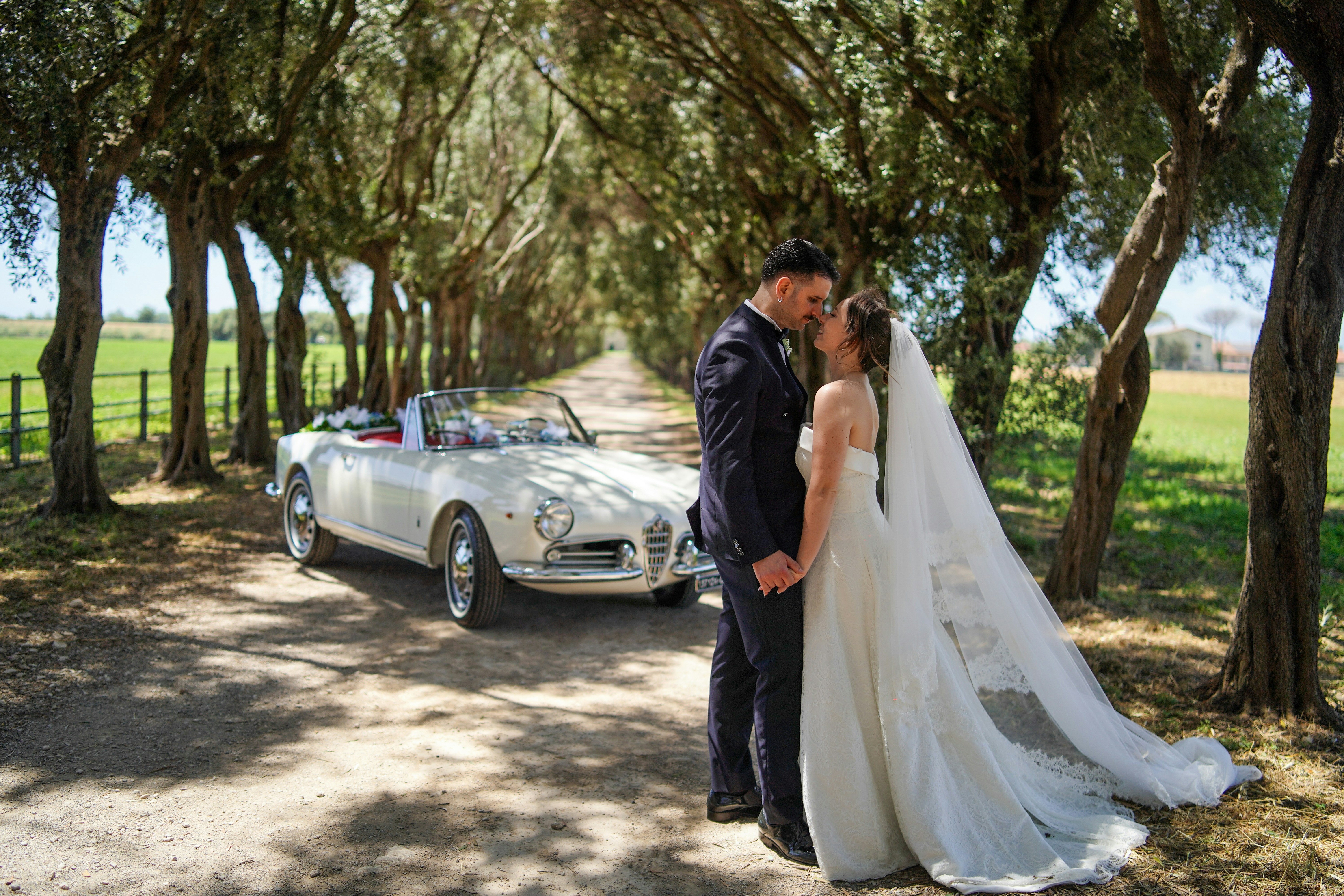 Bride and groom by vintage car on a tree-lined road