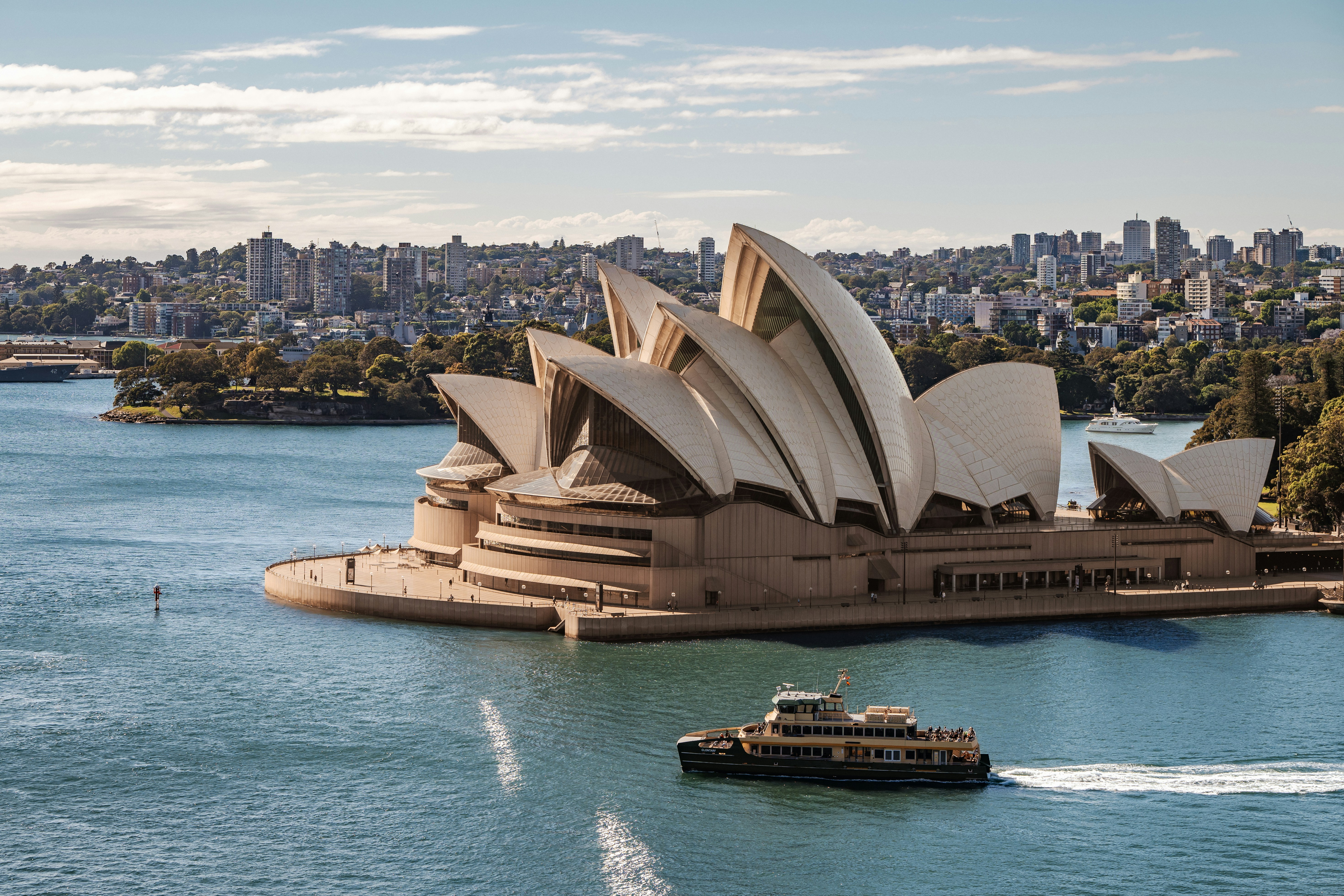 Sydney opera house and ferry on harbor with city skyline.
