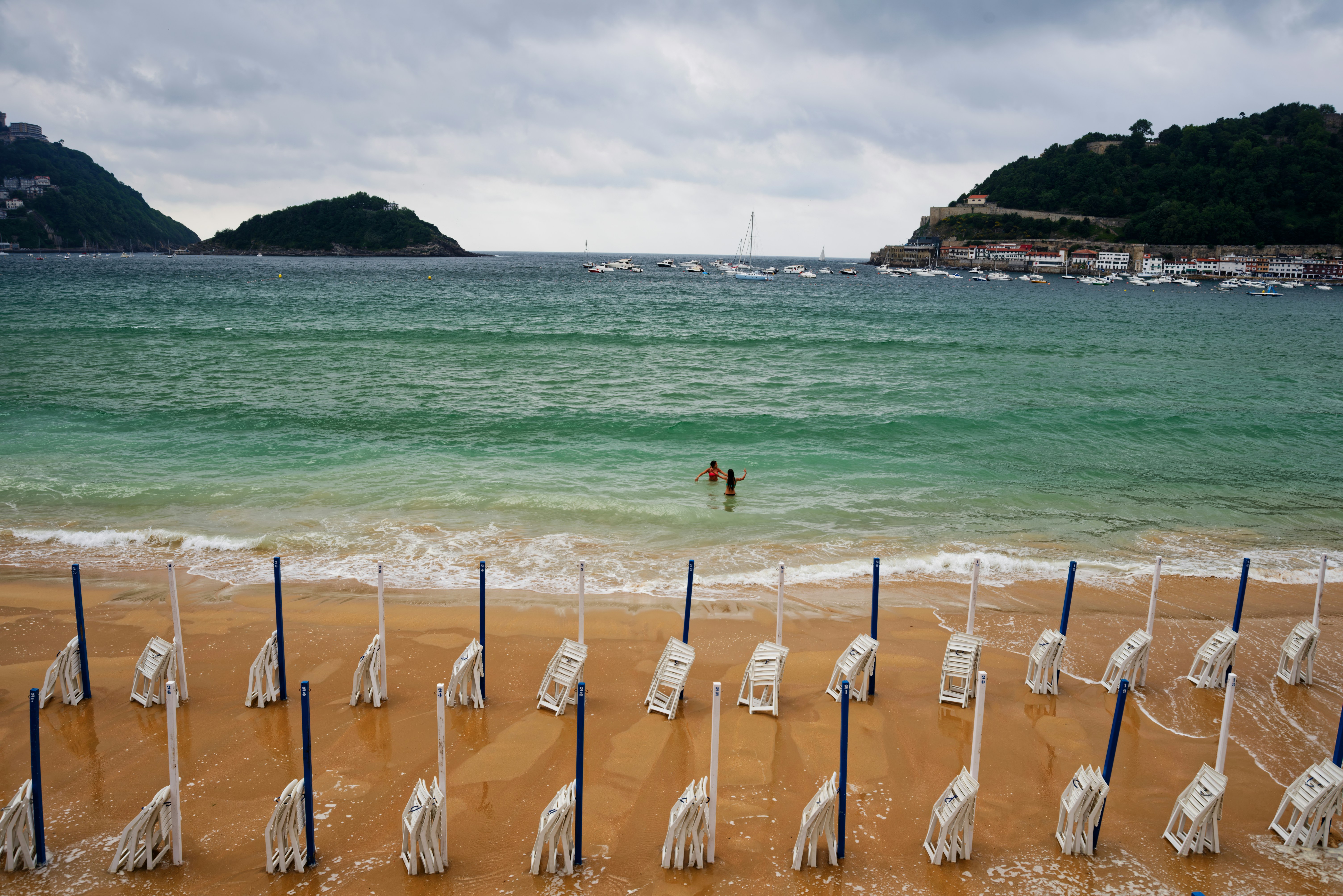 Beach with empty folded chairs and two people swimming