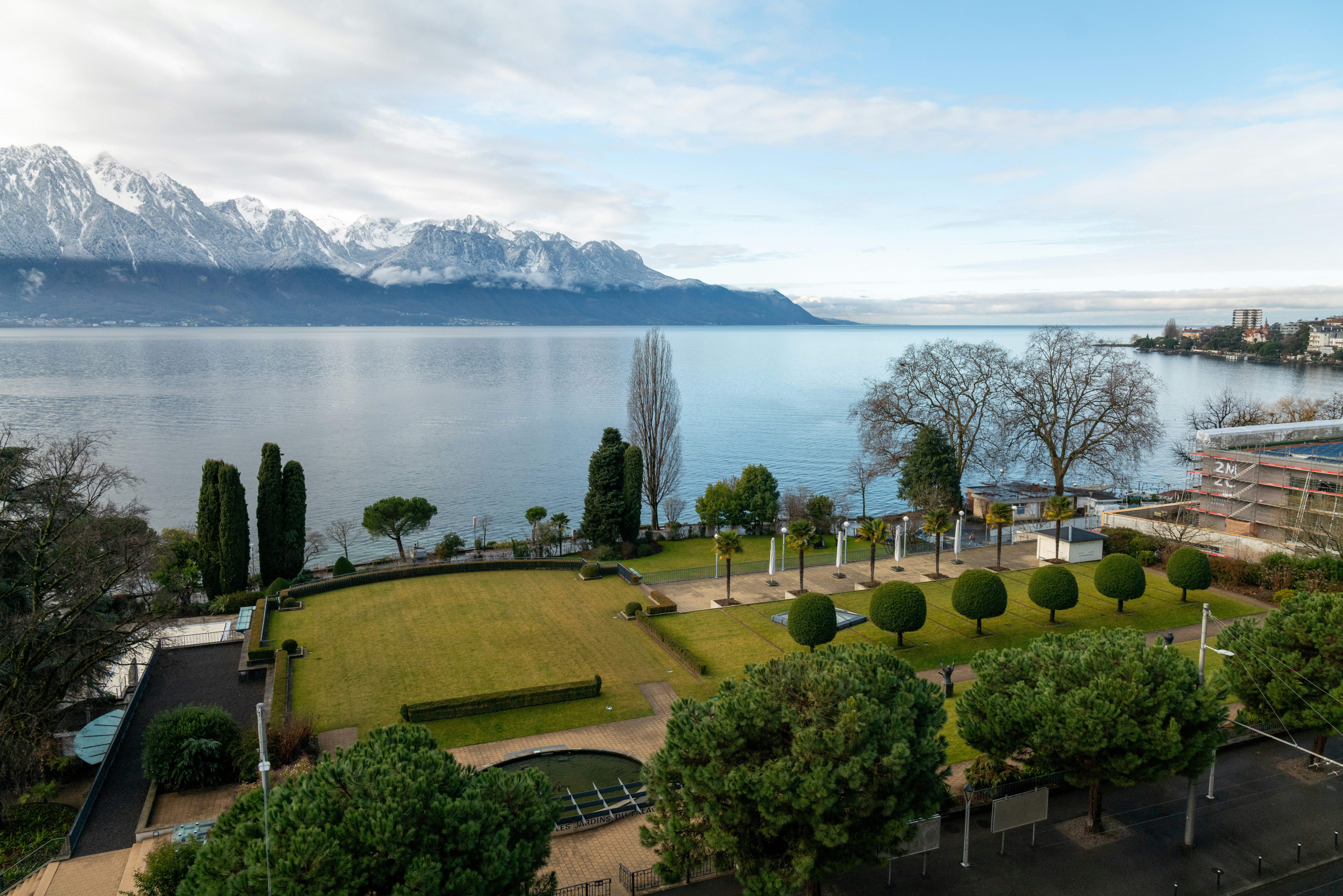 Scenic lake and garden with snow-capped mountains.