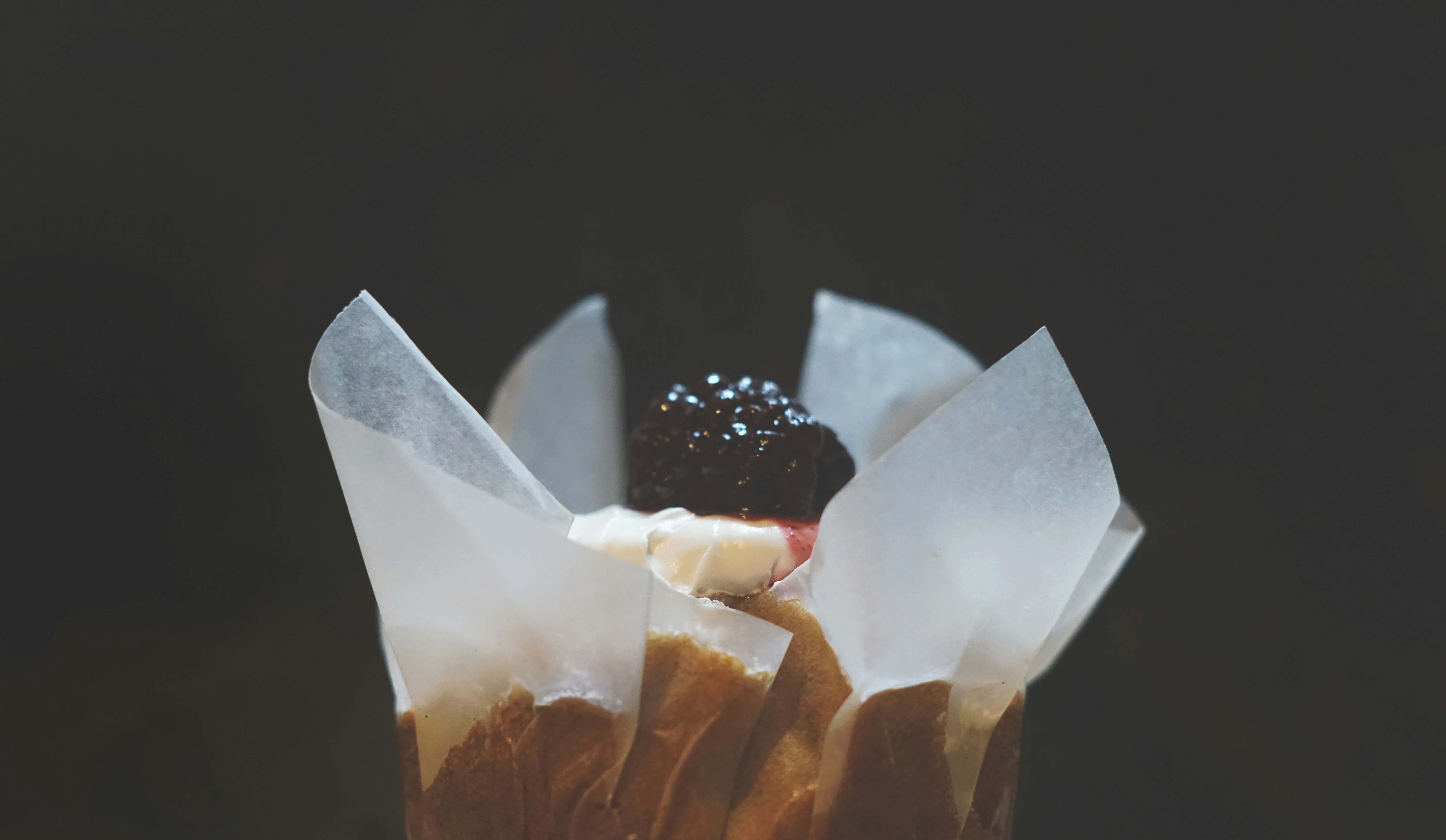 Cupcake with blackberry and cream in a paper wrapper.