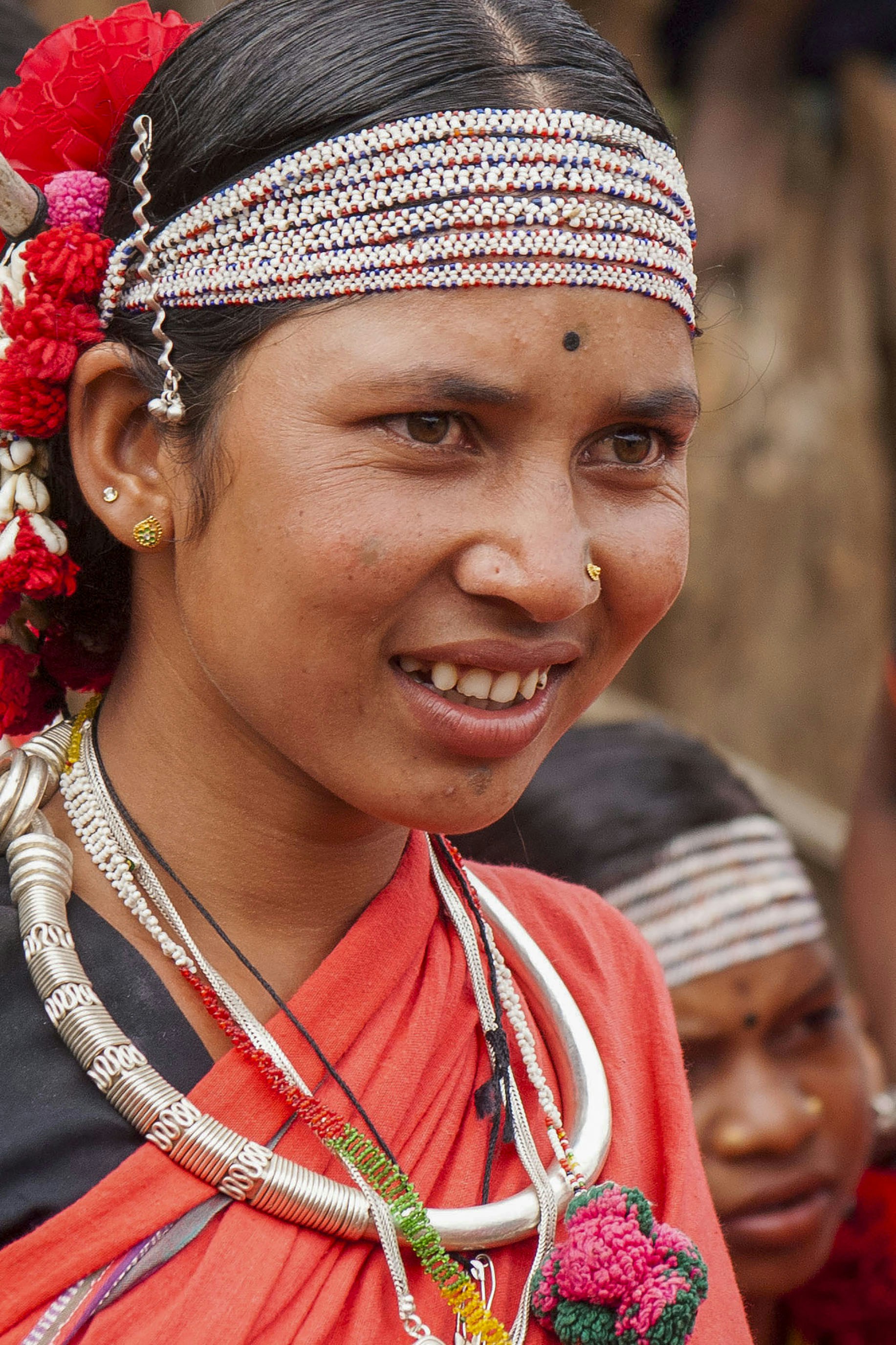 Mulher sorridente vestindo trajes tradicionais vermelhos, joias de prata e flores.