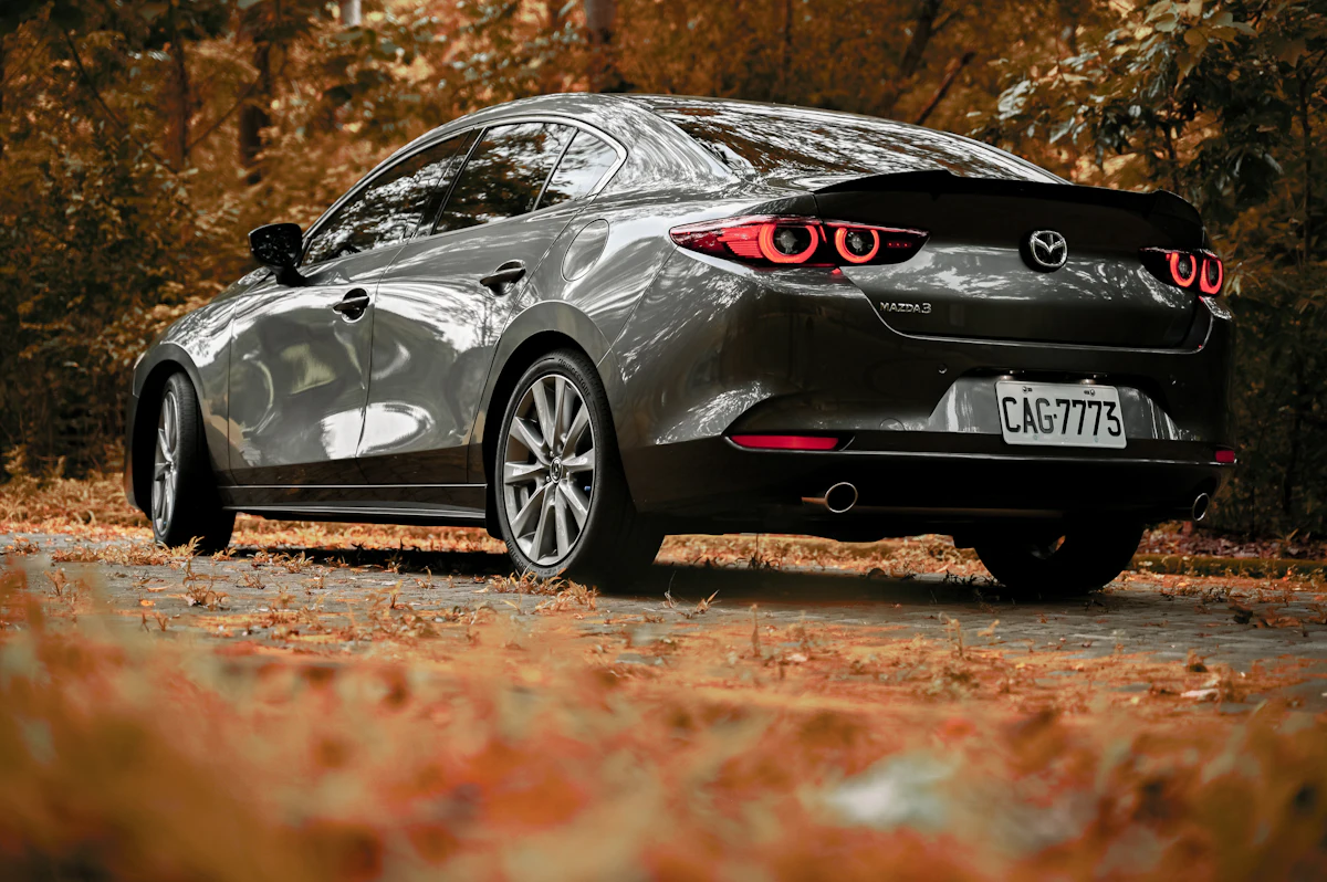 Sedán Mazda 3 gris oscuro estacionado en un camino con hojas de otoño