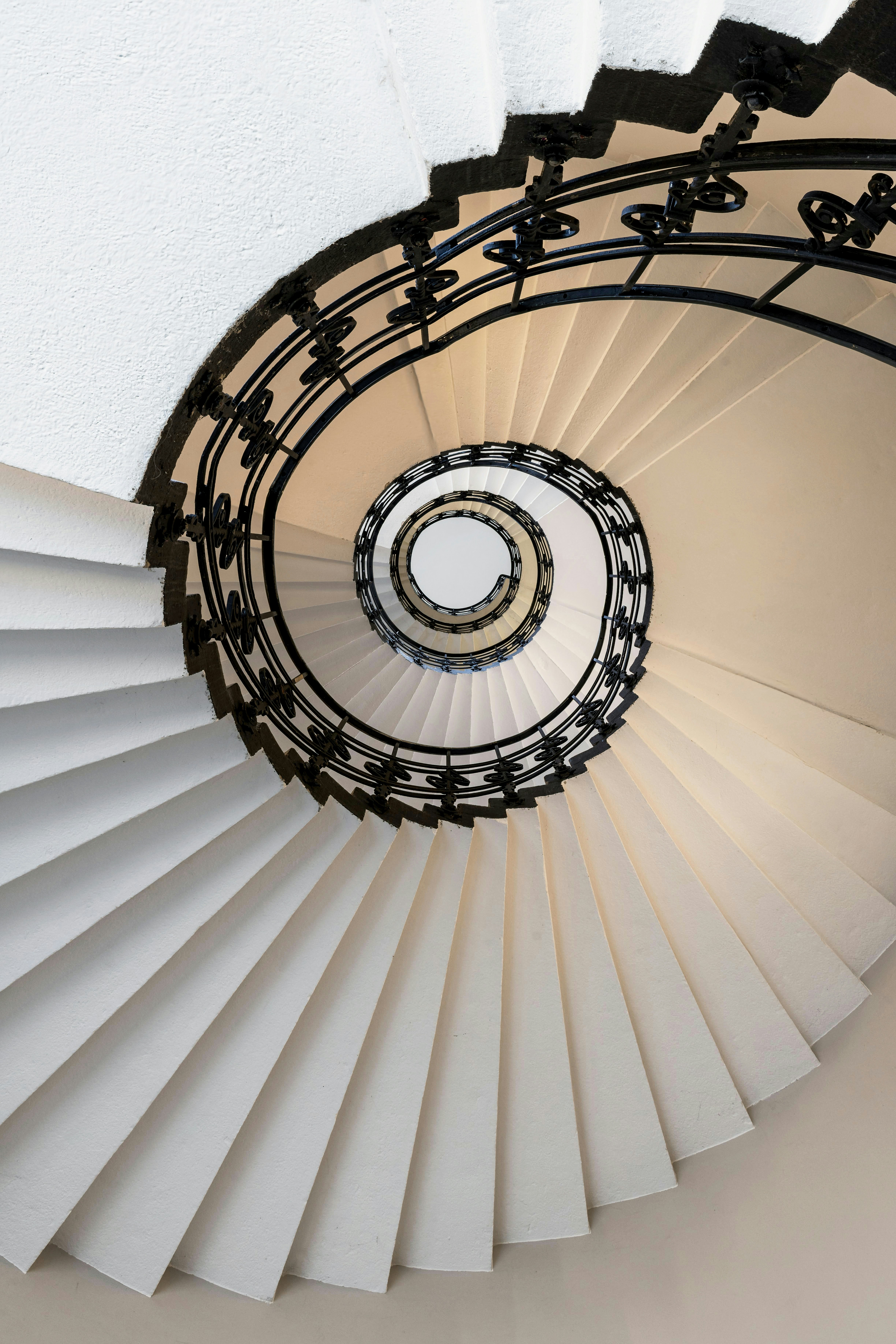 A white spiral staircase with ornate black railing from above.