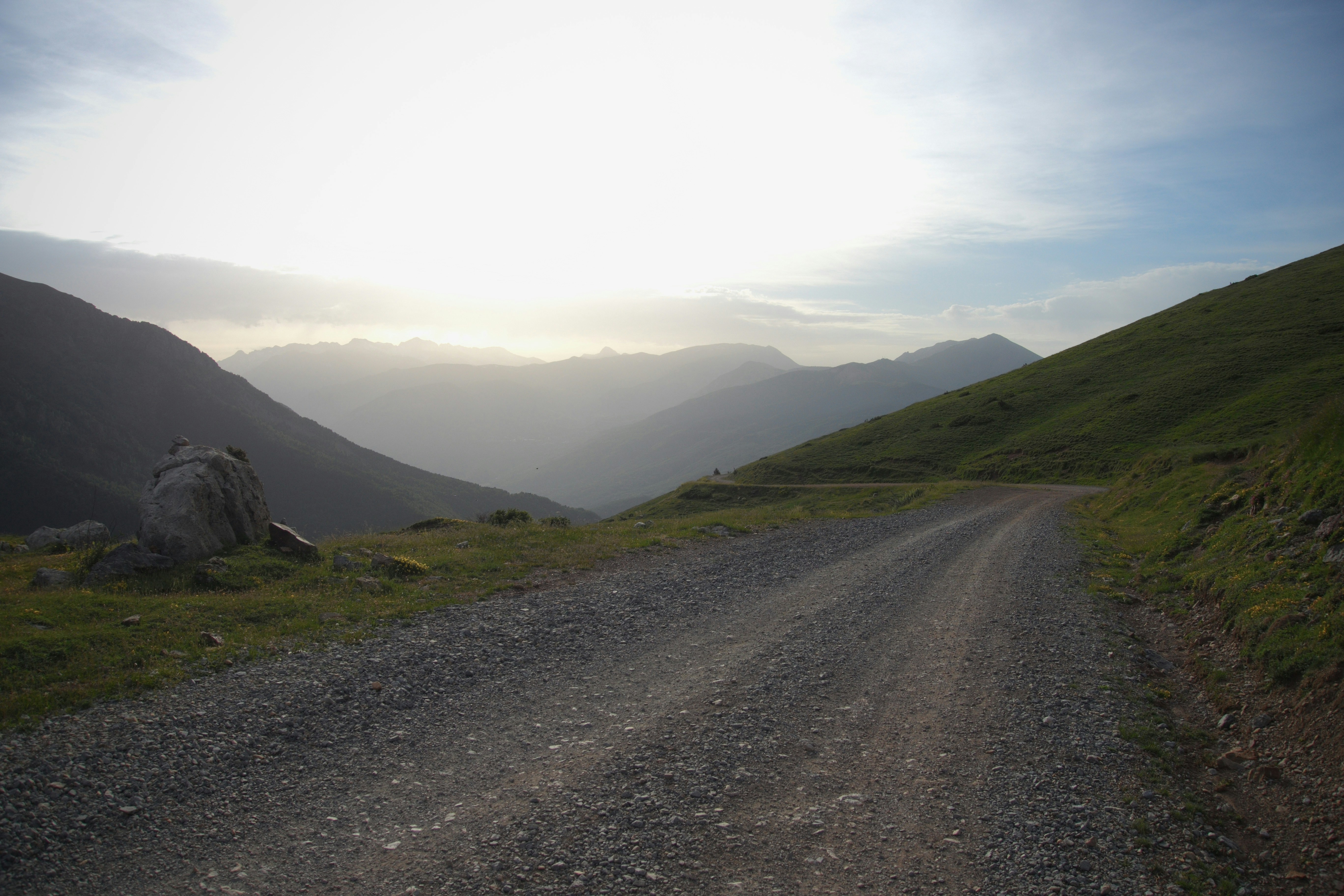 A gravel road winding through a mountain valley at sunset.