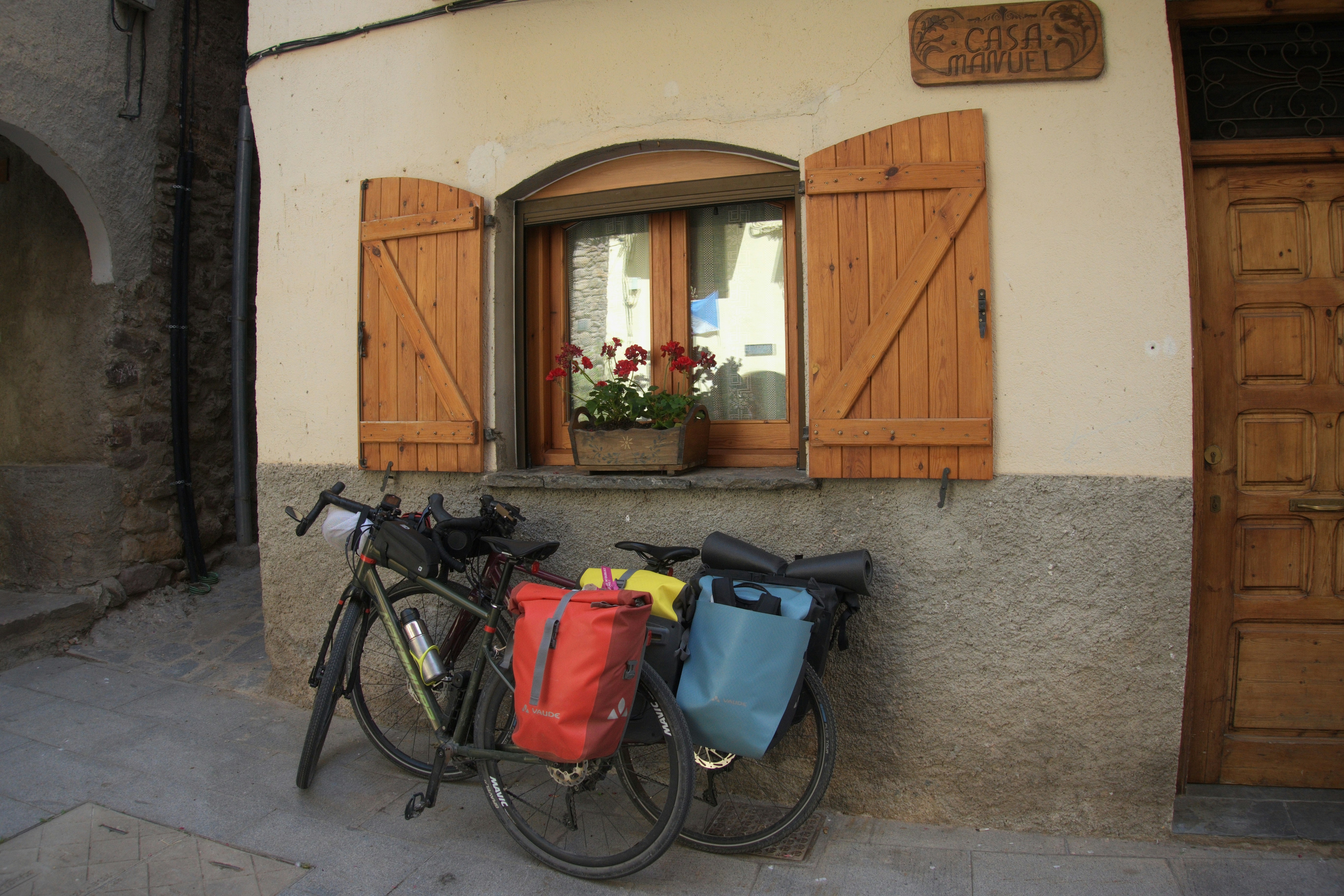 Two touring bicycles parked against a rustic building with shutters.
