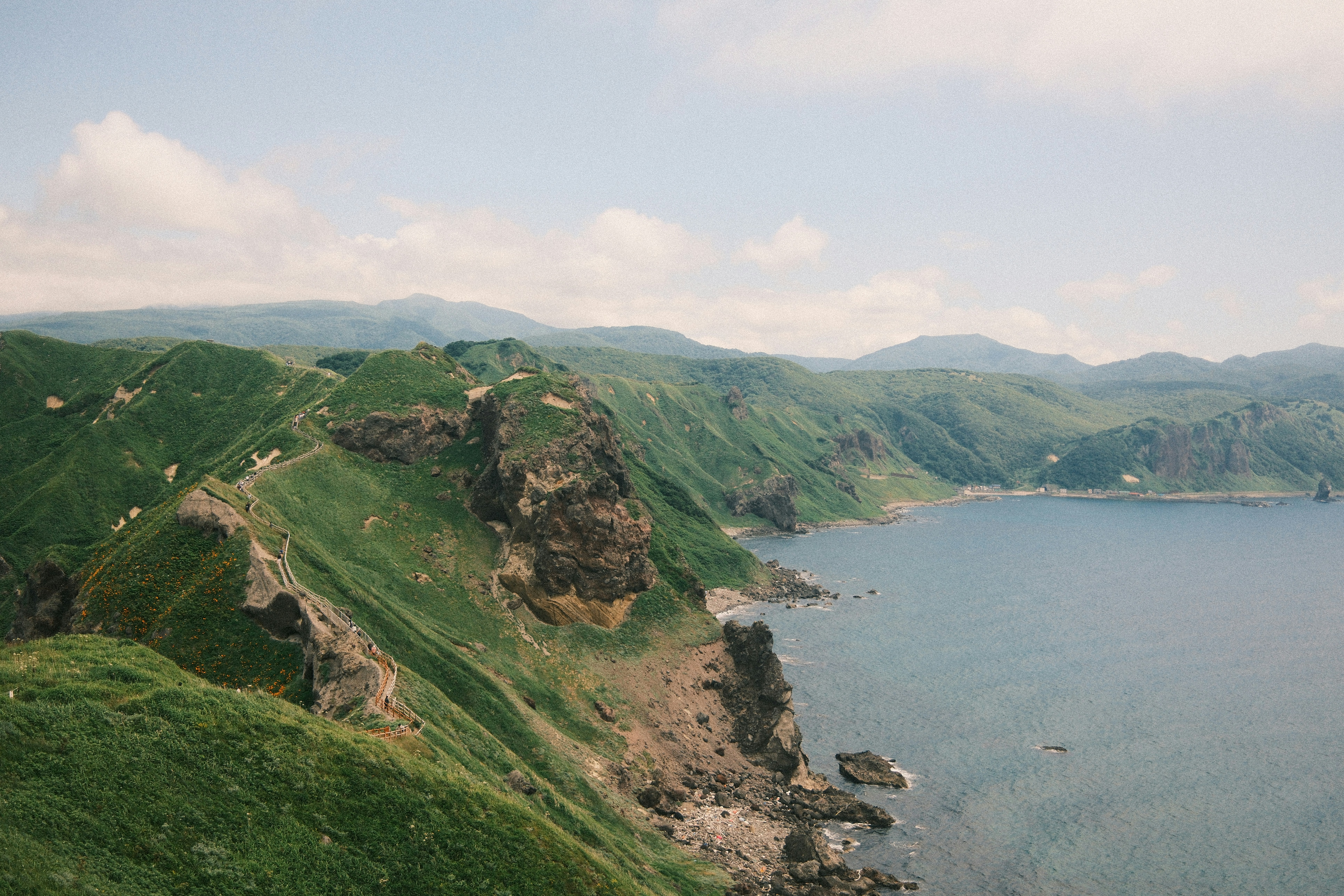 Green coastal cliffs meet the ocean under a clear sky.