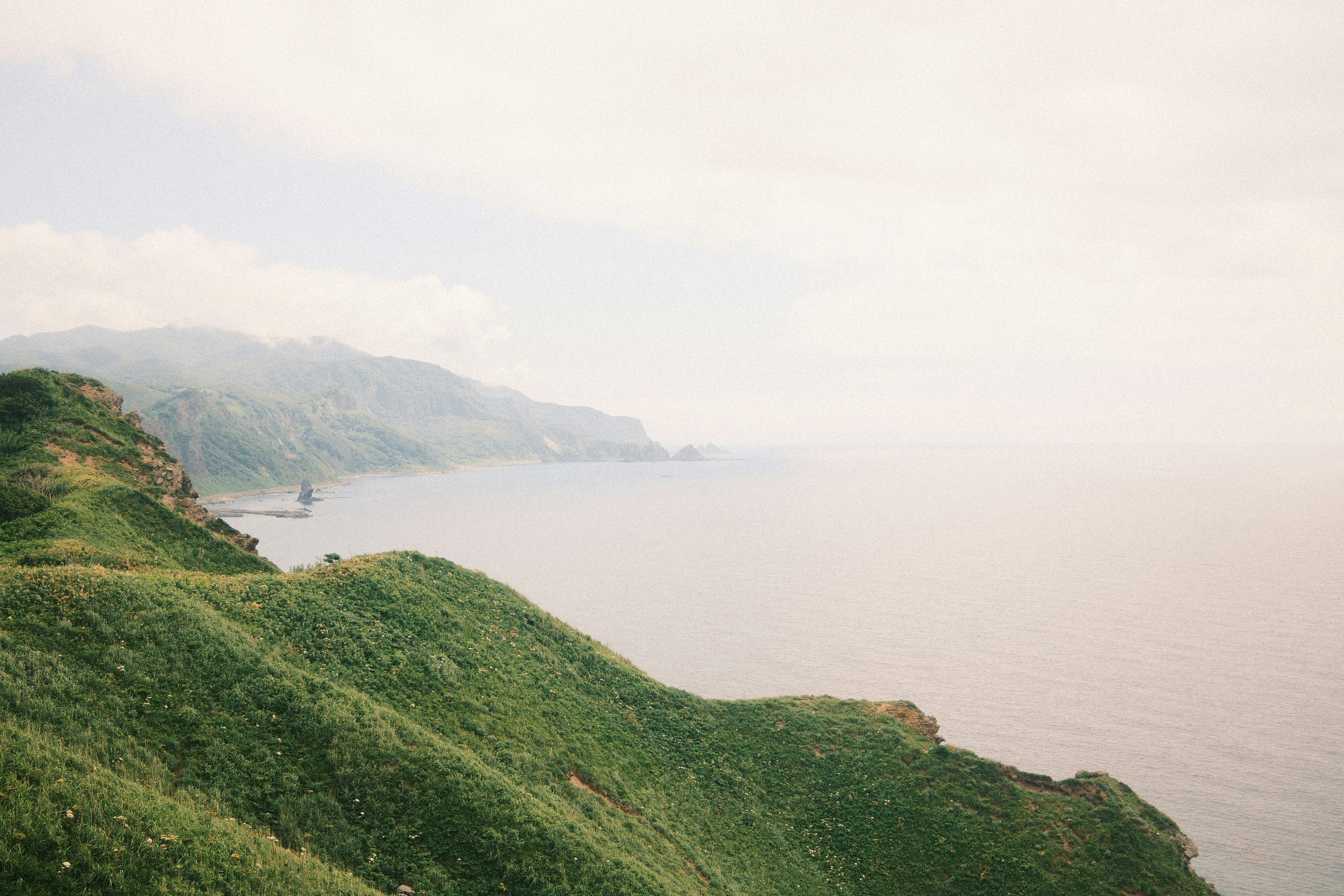 Green hills meet the ocean under a hazy sky