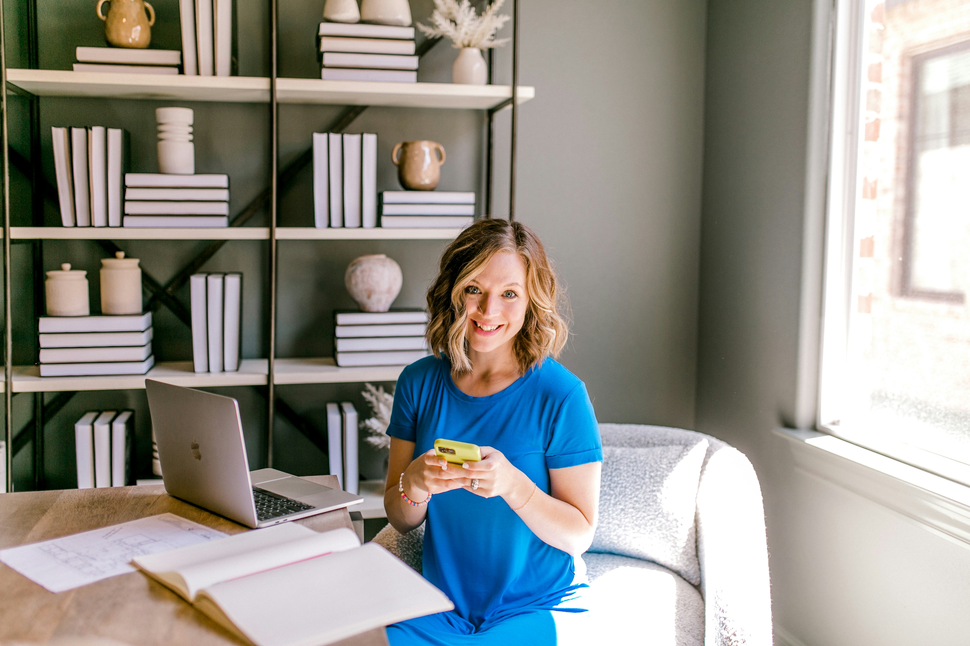 Smiling woman holding a phone at a desk with books