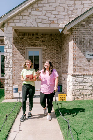 Smiling women walk together on a path towards a house.