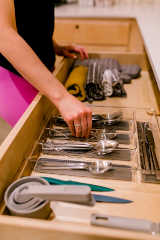 A hand organizing silverware in a kitchen drawer.