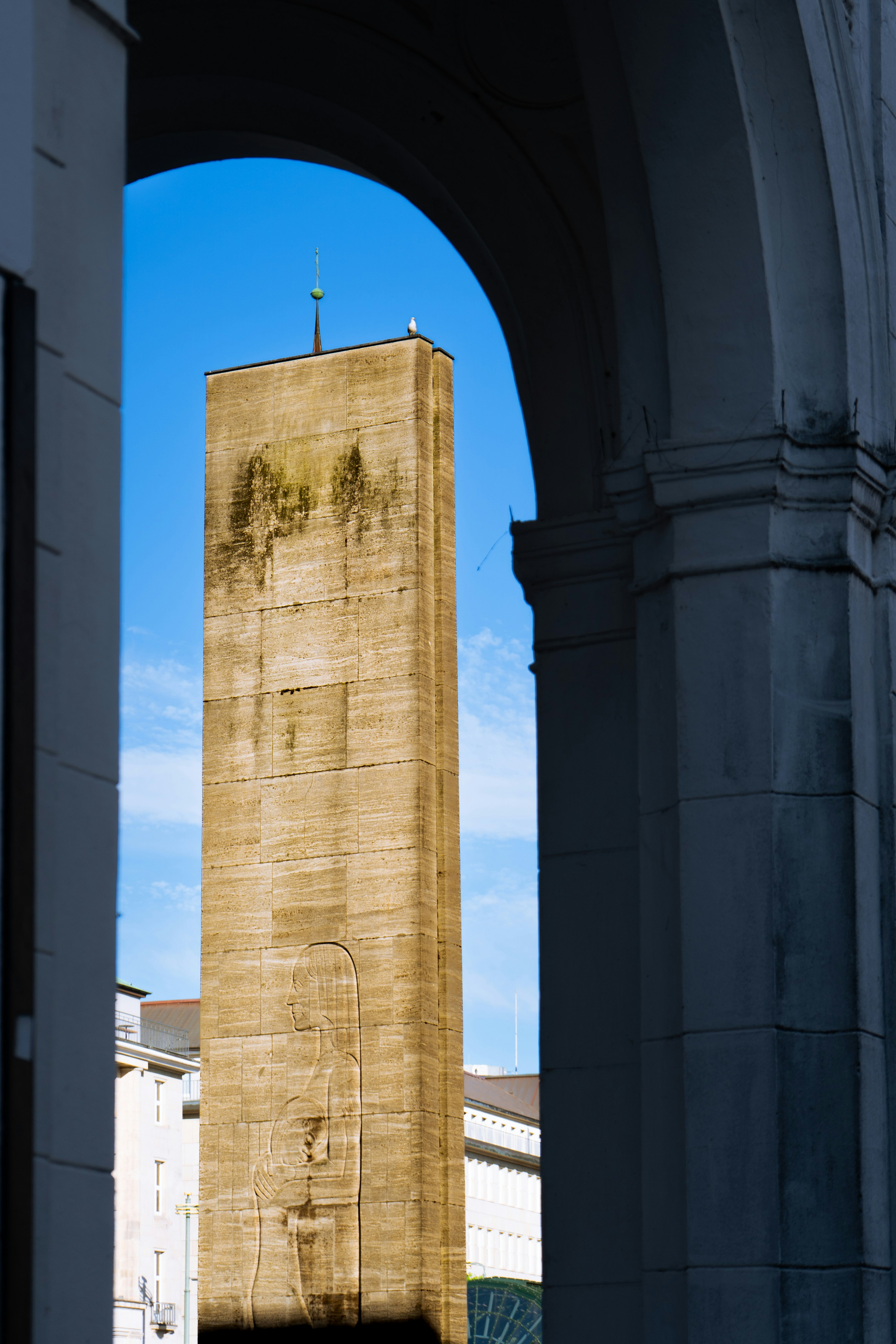 Weathered concrete tower framed by arches under blue sky.
