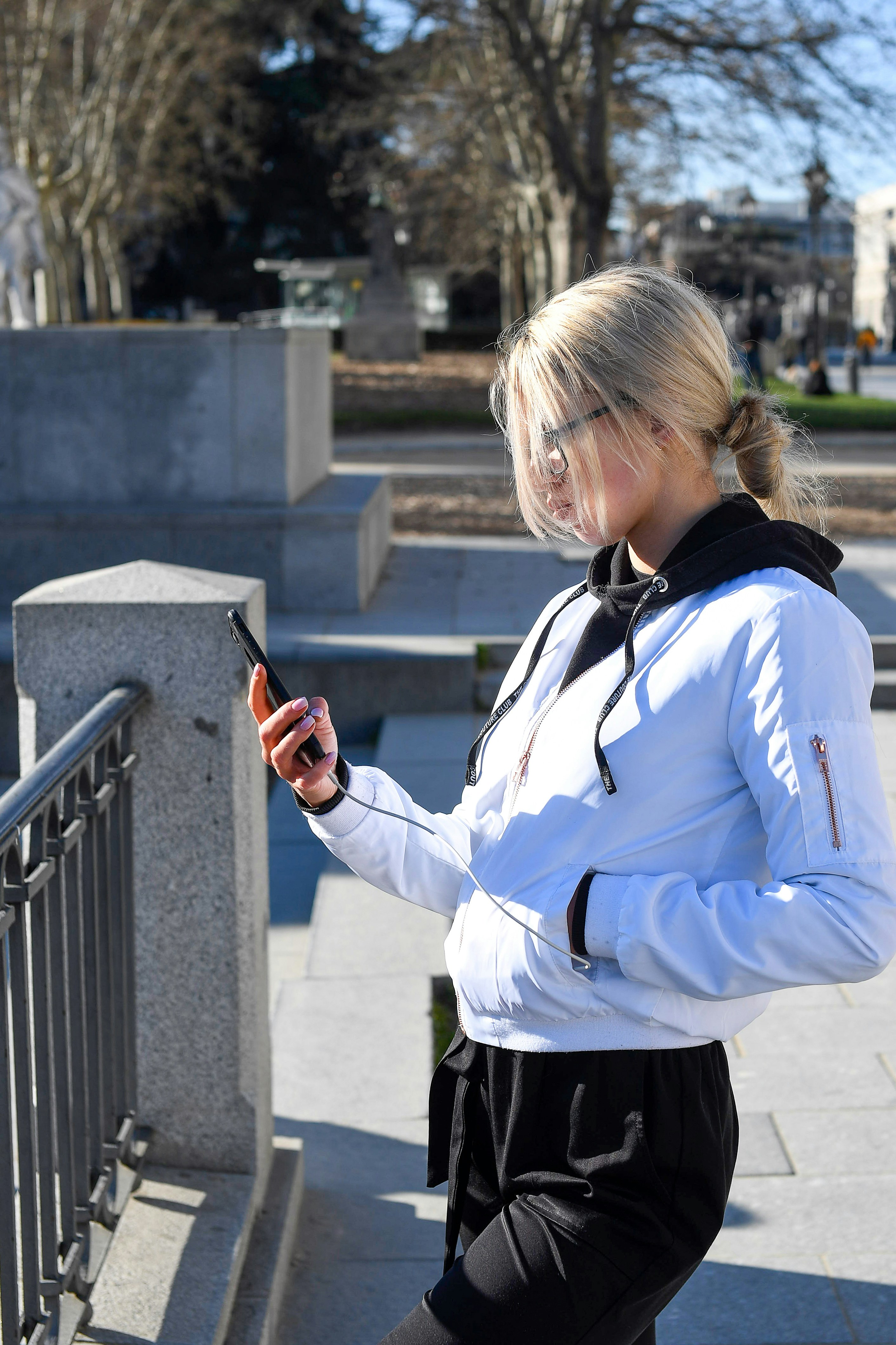 Blonde woman in white jacket looking at her smartphone outside.