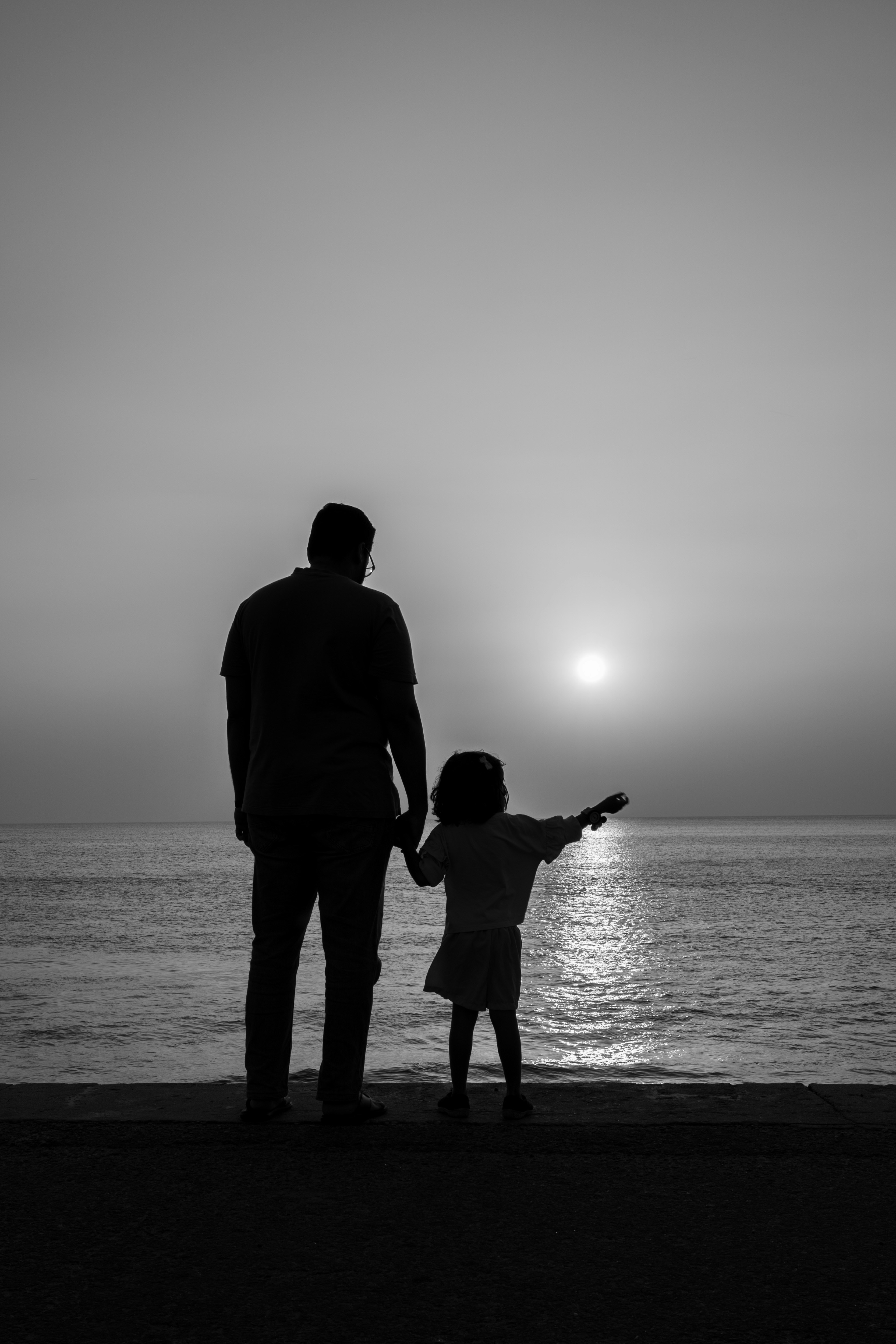 Father and child silhouetted against a sunset over the ocean