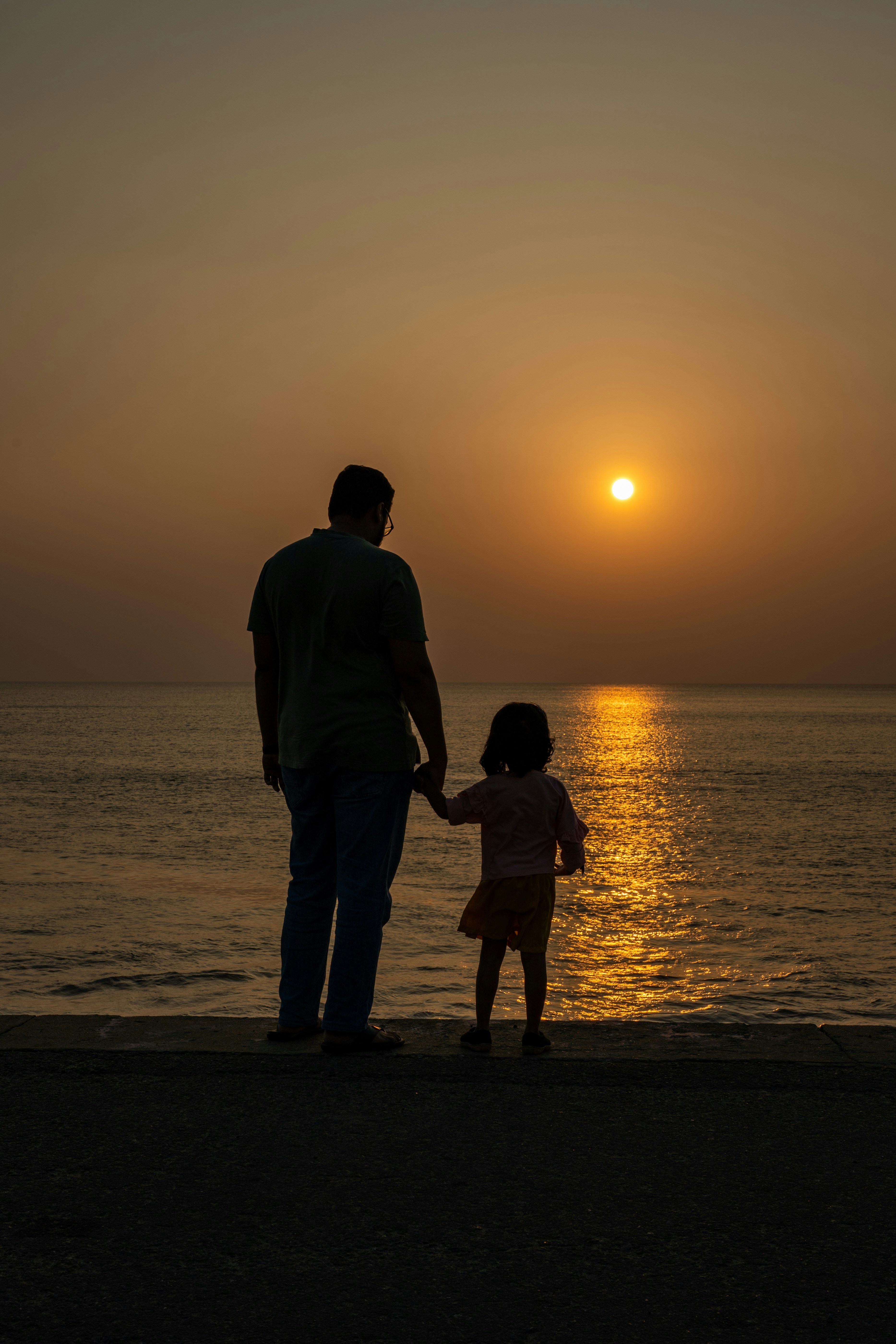 Pai e filho de mãos dadas assistindo ao pôr do sol sobre o oceano ...