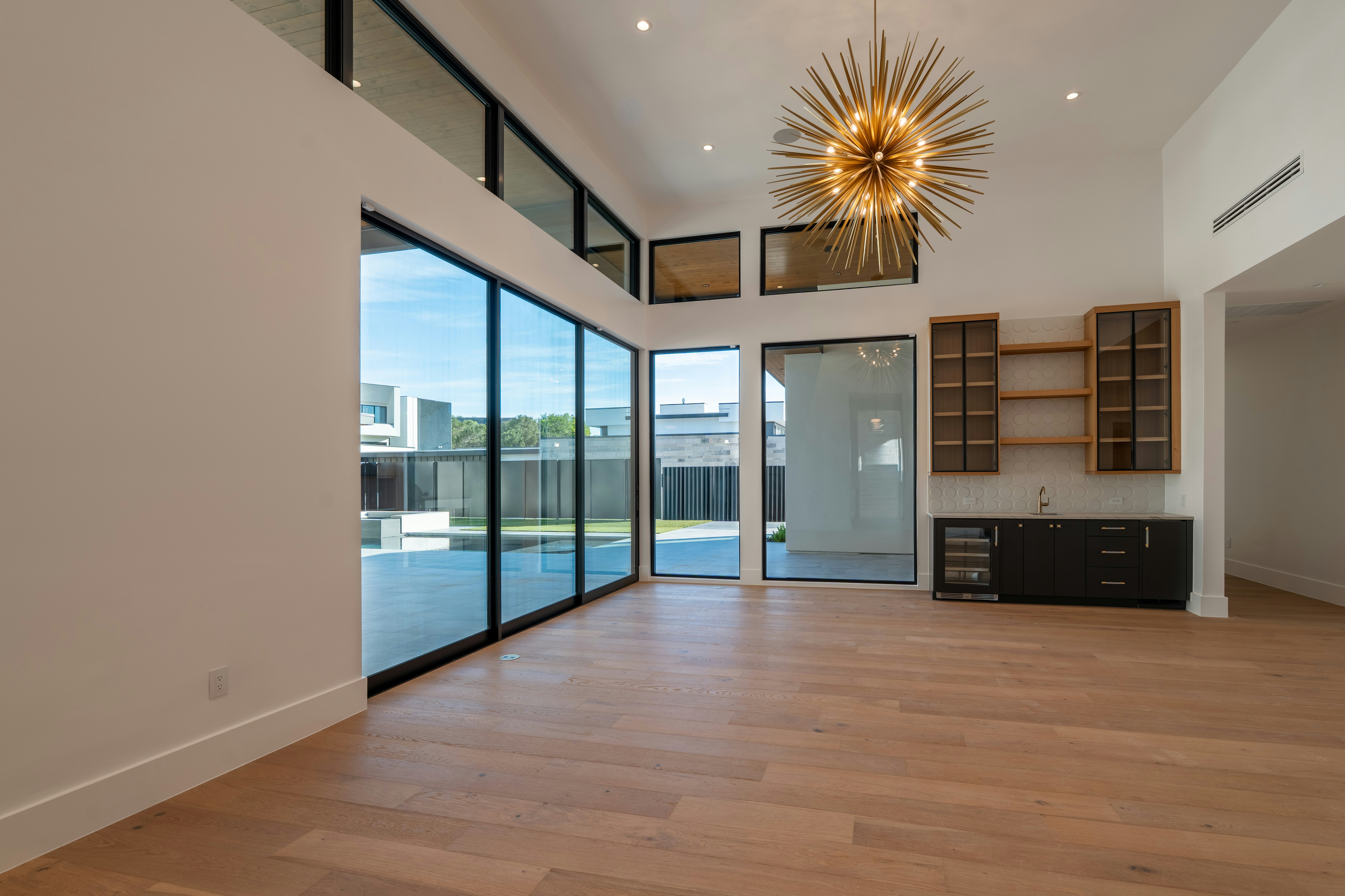 Modern empty room with glass doors, high ceilings, and chandelier.