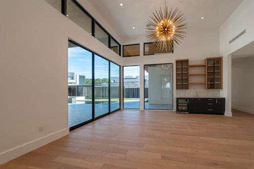 Modern empty room with glass doors, high ceilings, and chandelier