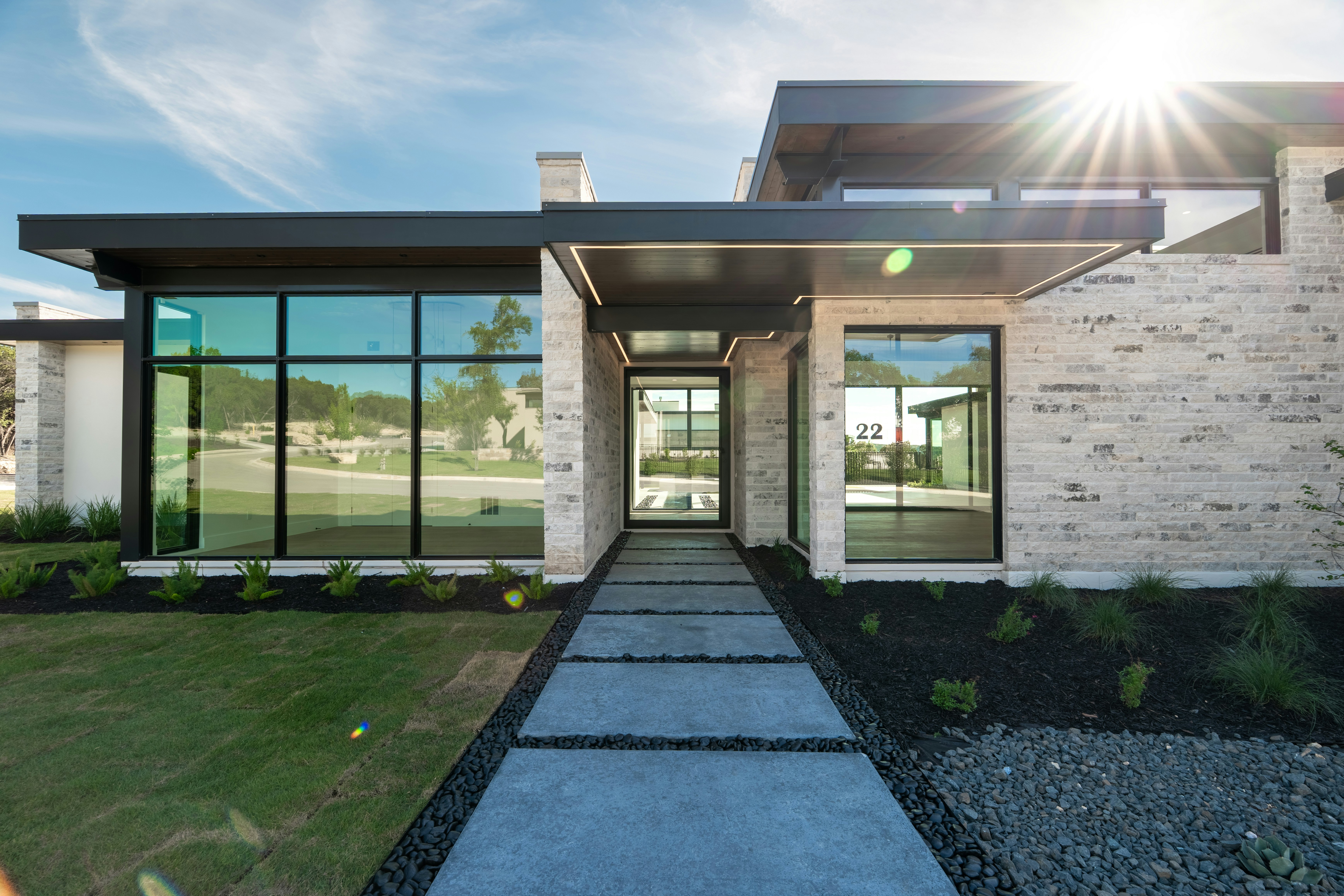 Contemporary home with stone facade, large windows, and sun flare.