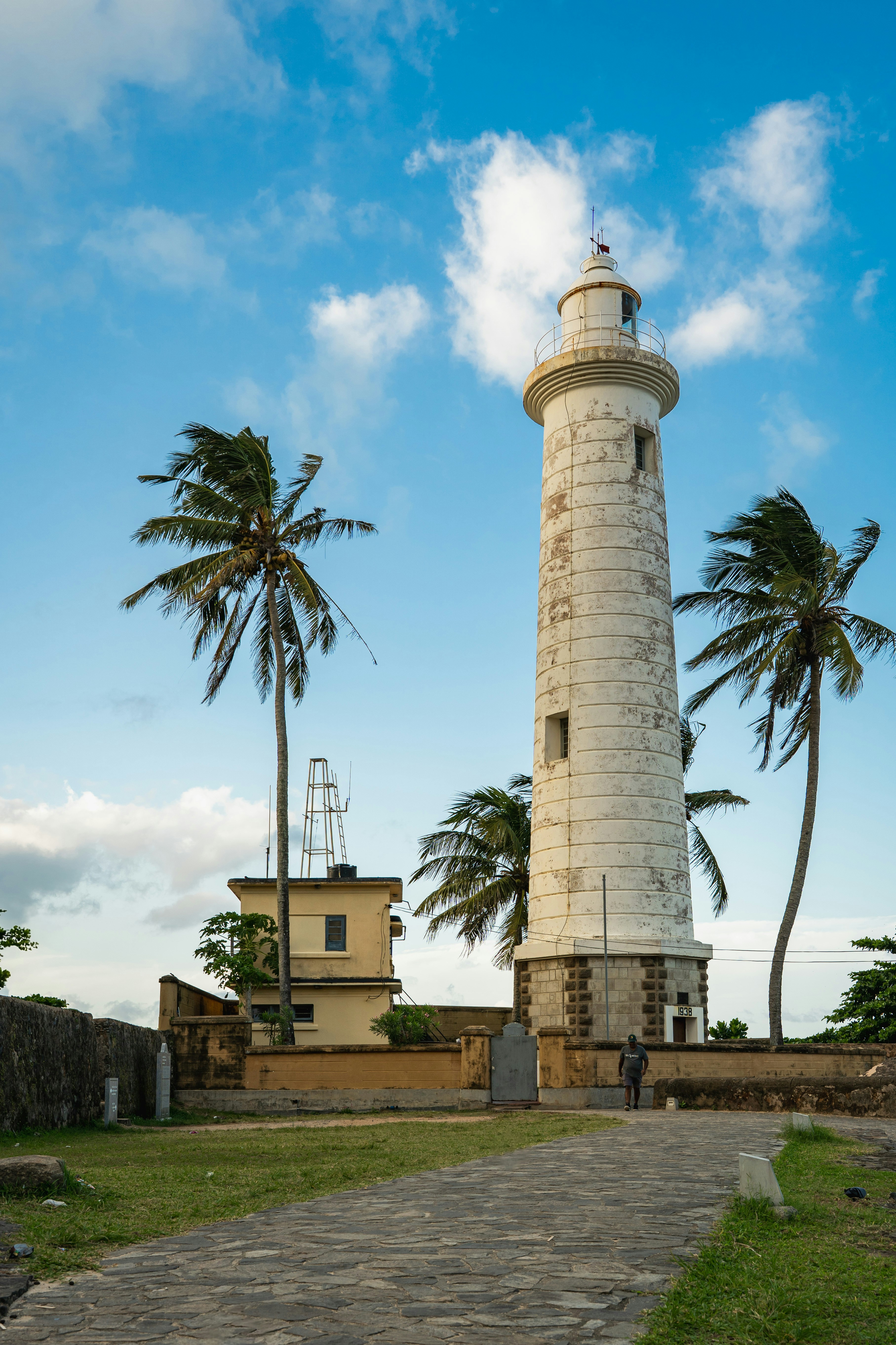 Historic white lighthouse with palm trees against a blue sky