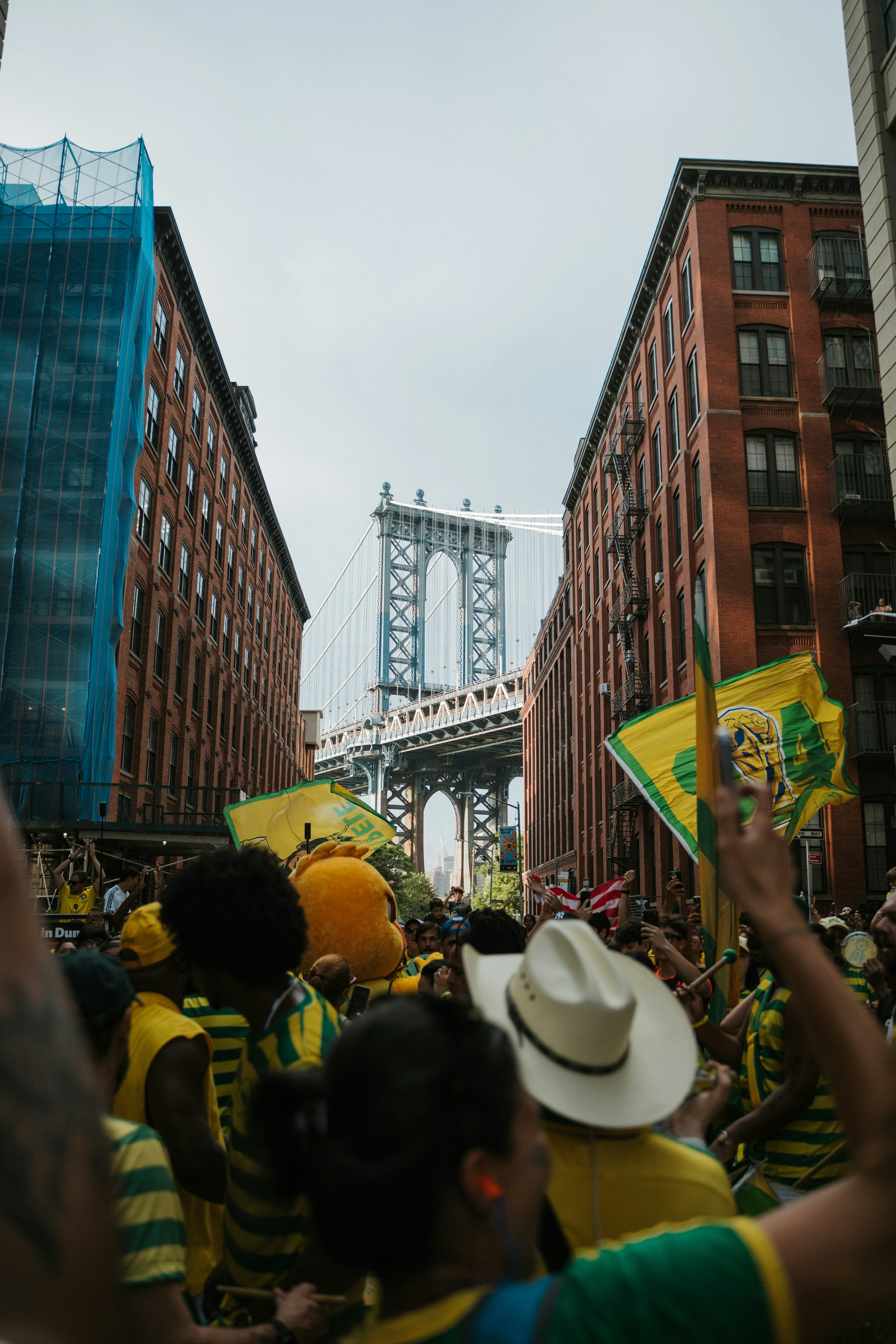 Multidão festiva com bandeiras sob a icônica ponte de Manhattan.
