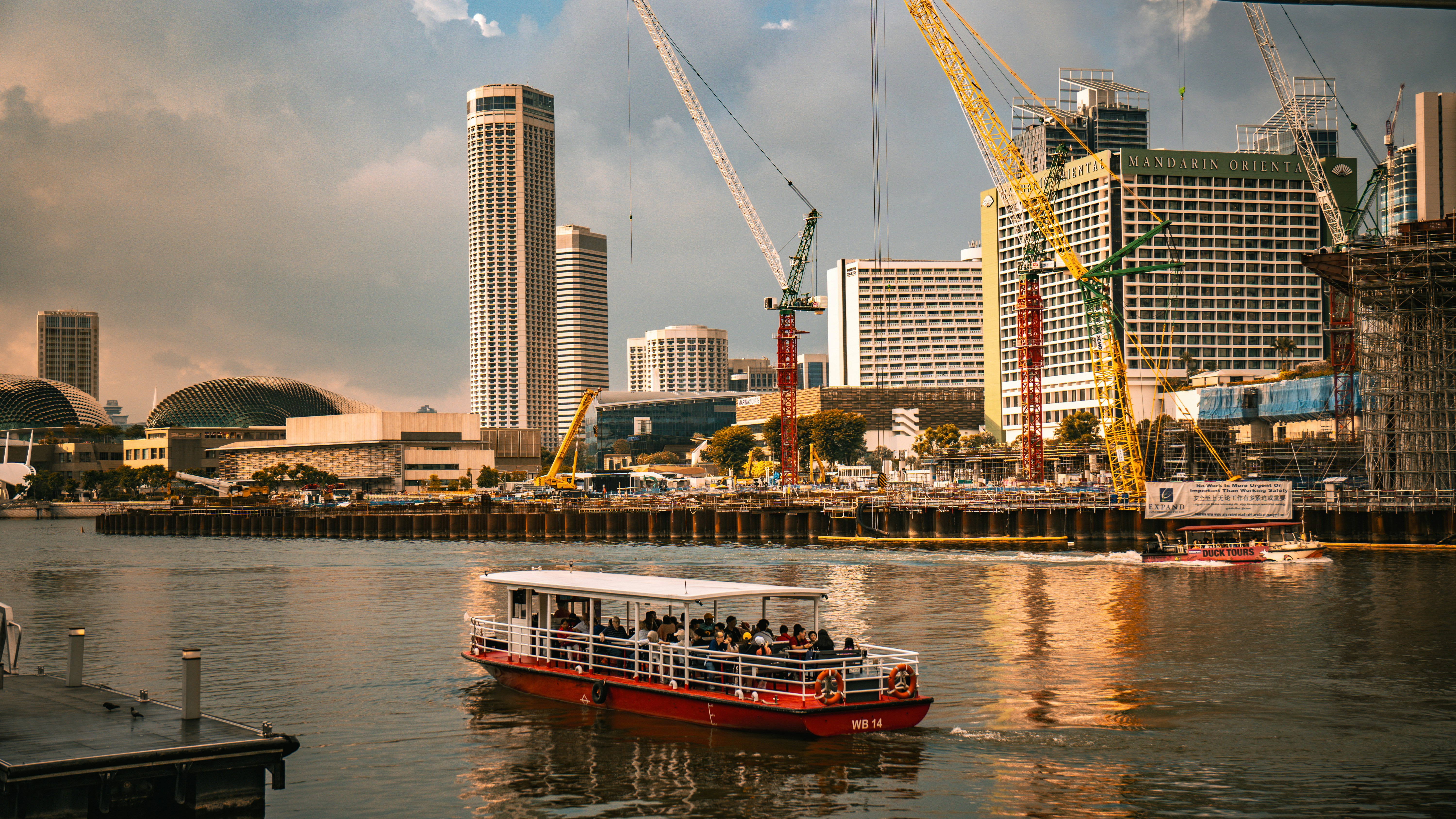 Rotes Tourboot auf dem Wasser mit Stadtsilhouette und Kränen.