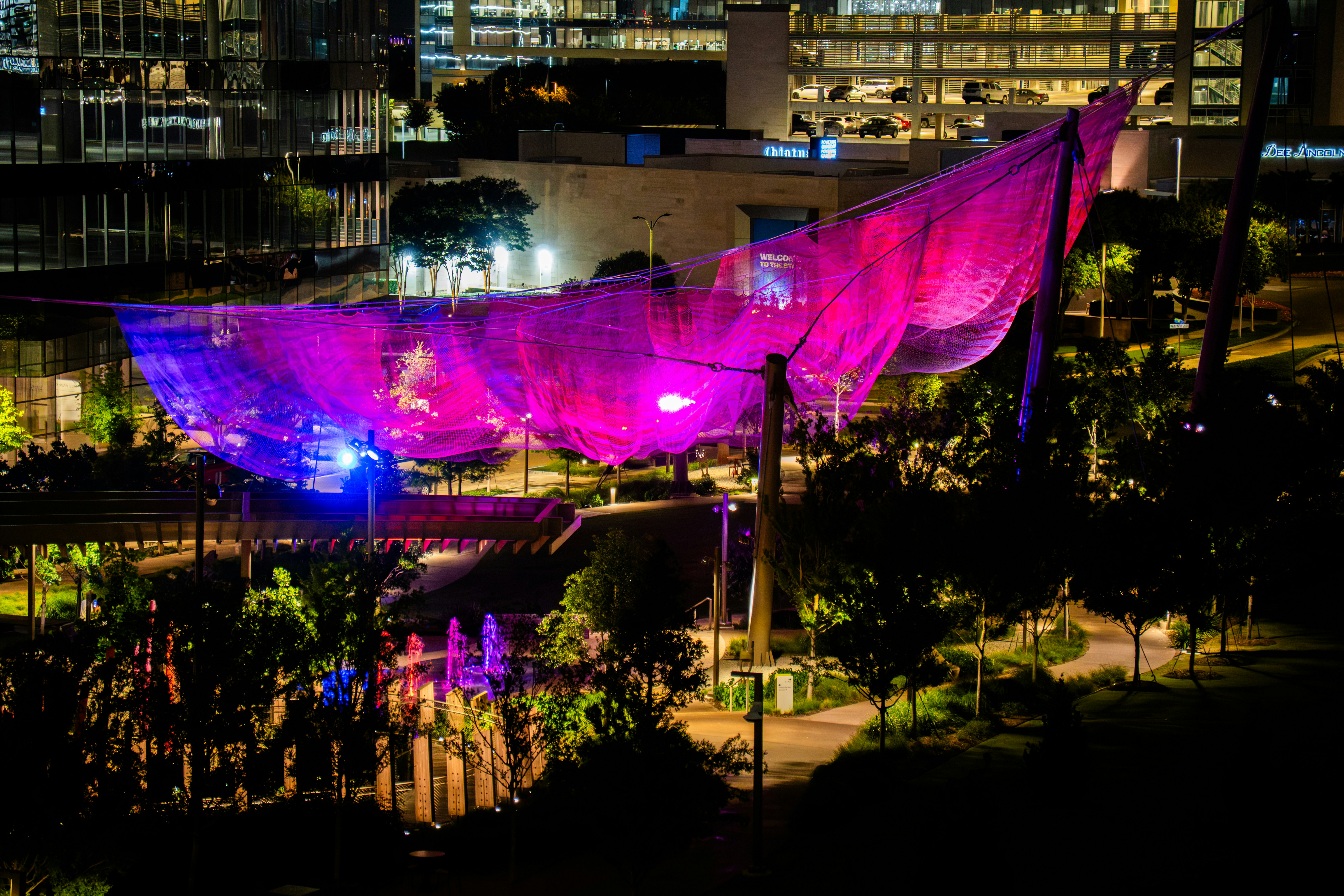 Vibrant illuminated net sculpture over a park at night