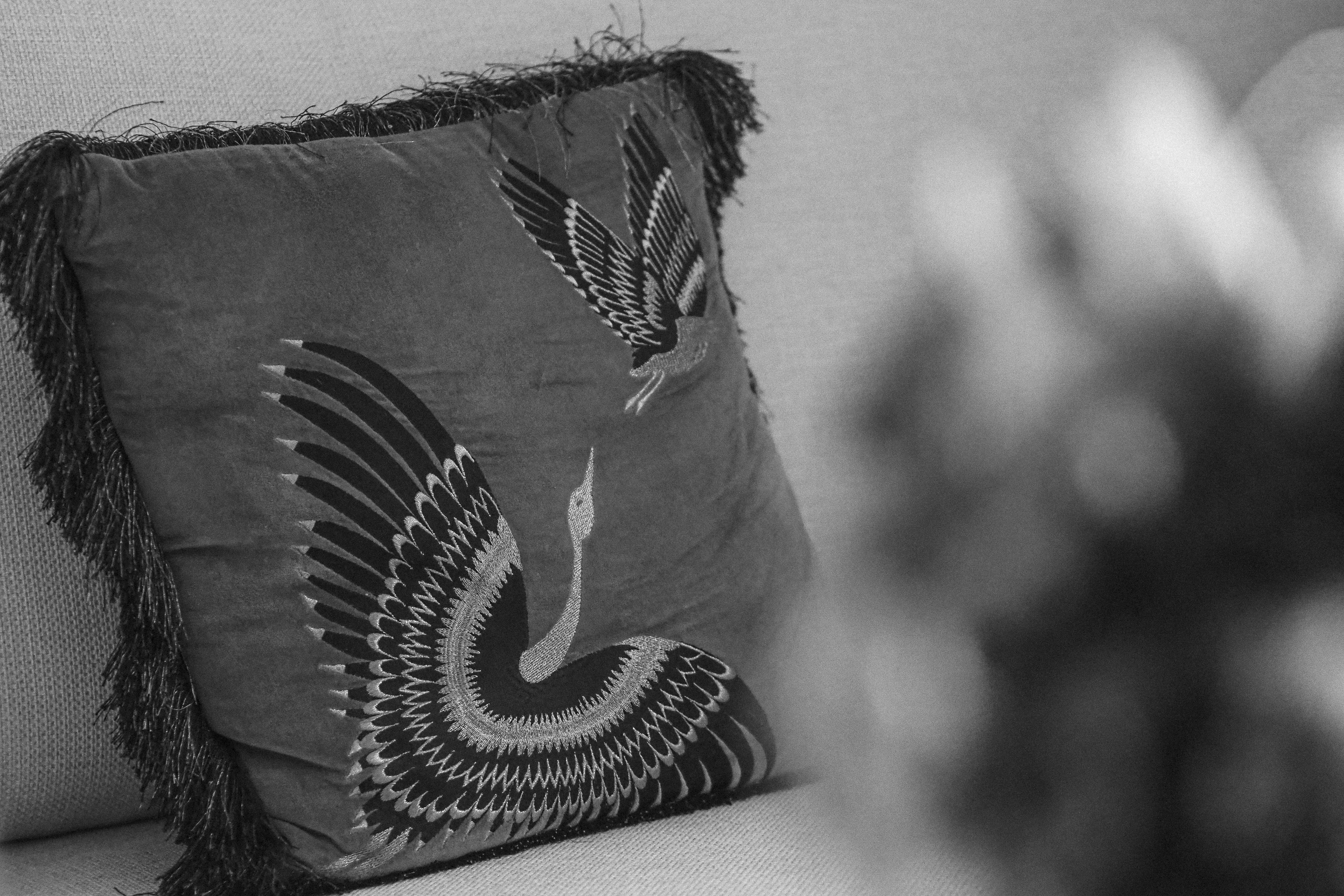 A decorative pillow with a bird design and fringe.