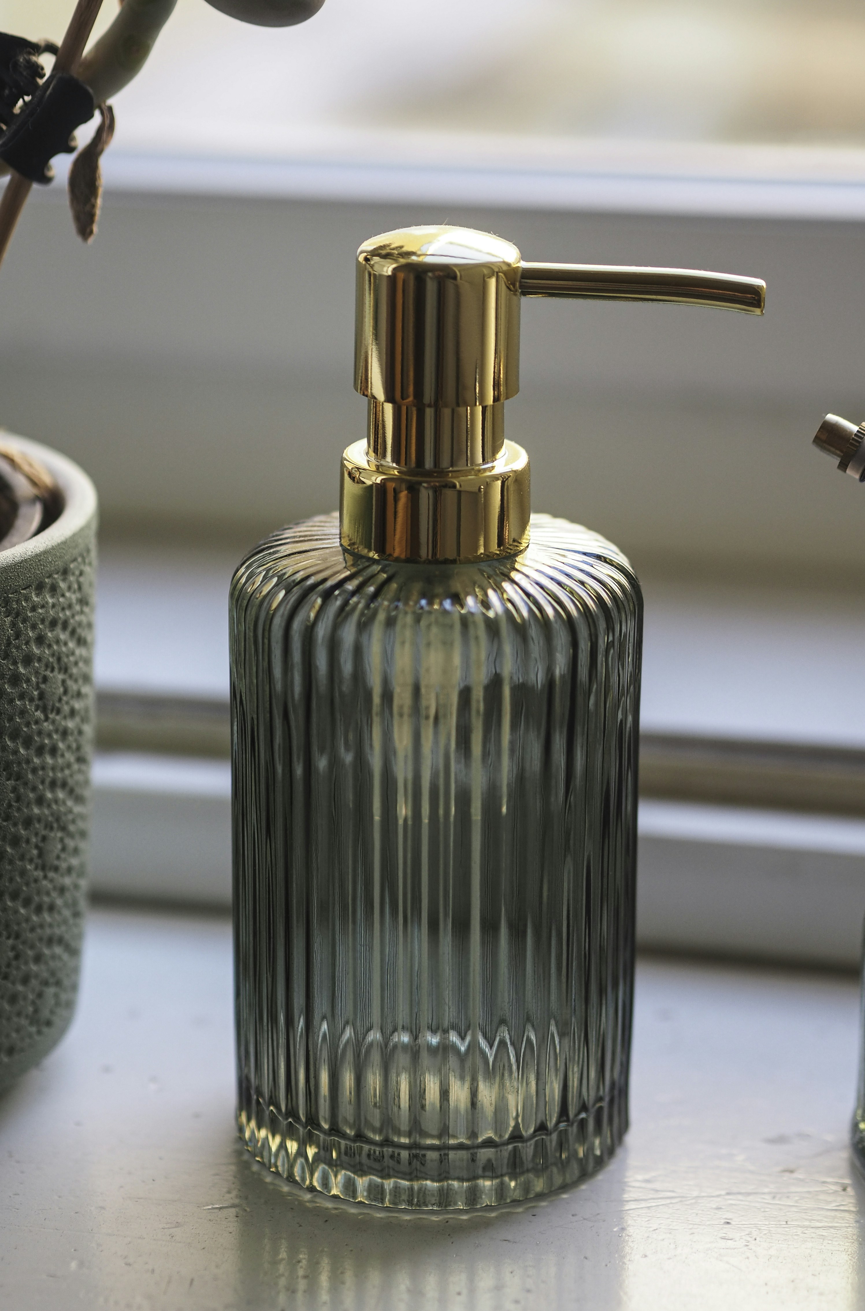 Ribbed glass soap dispenser with gold pump on a windowsill