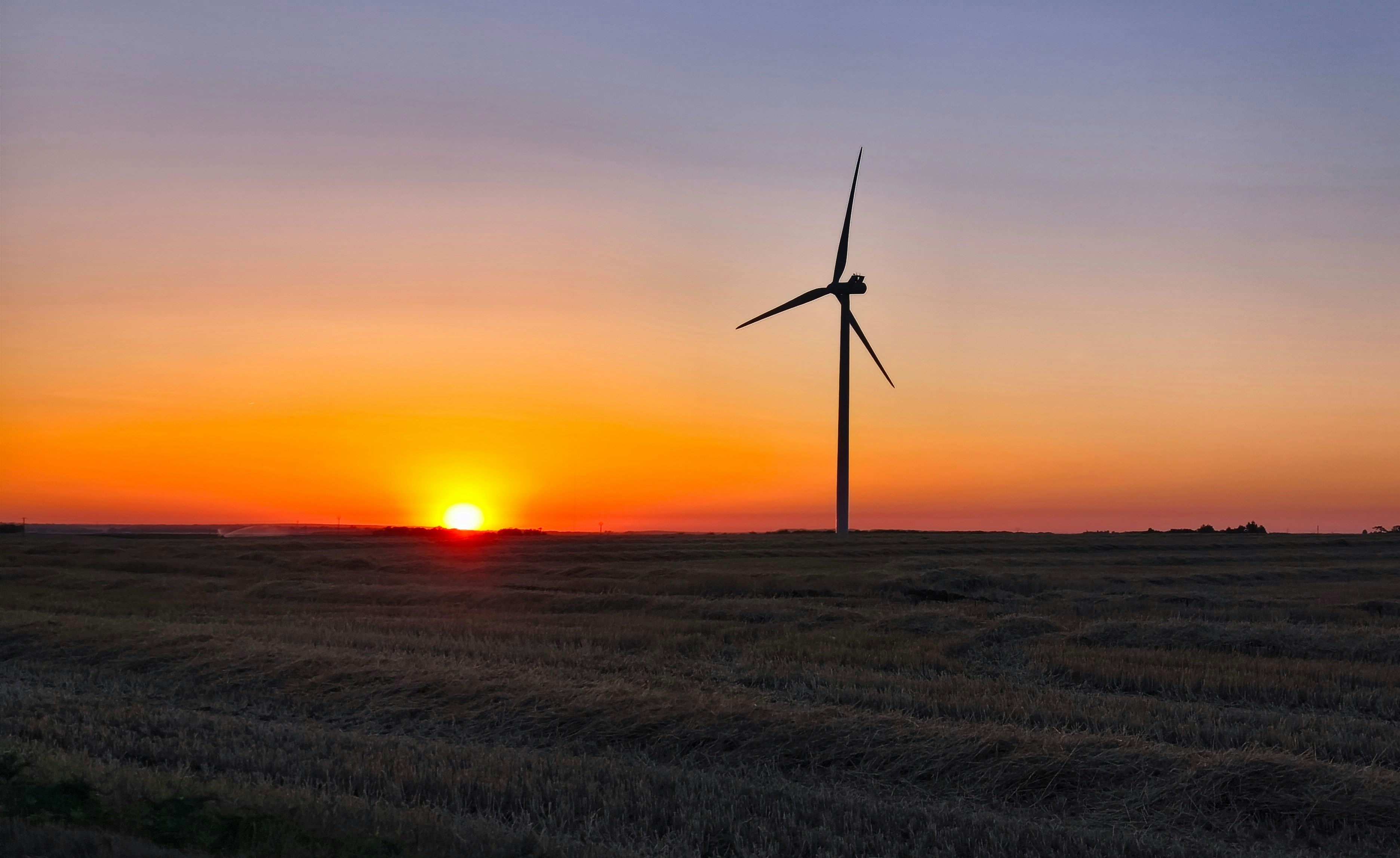 Wind turbine silhouette against a vibrant sunset over a field.