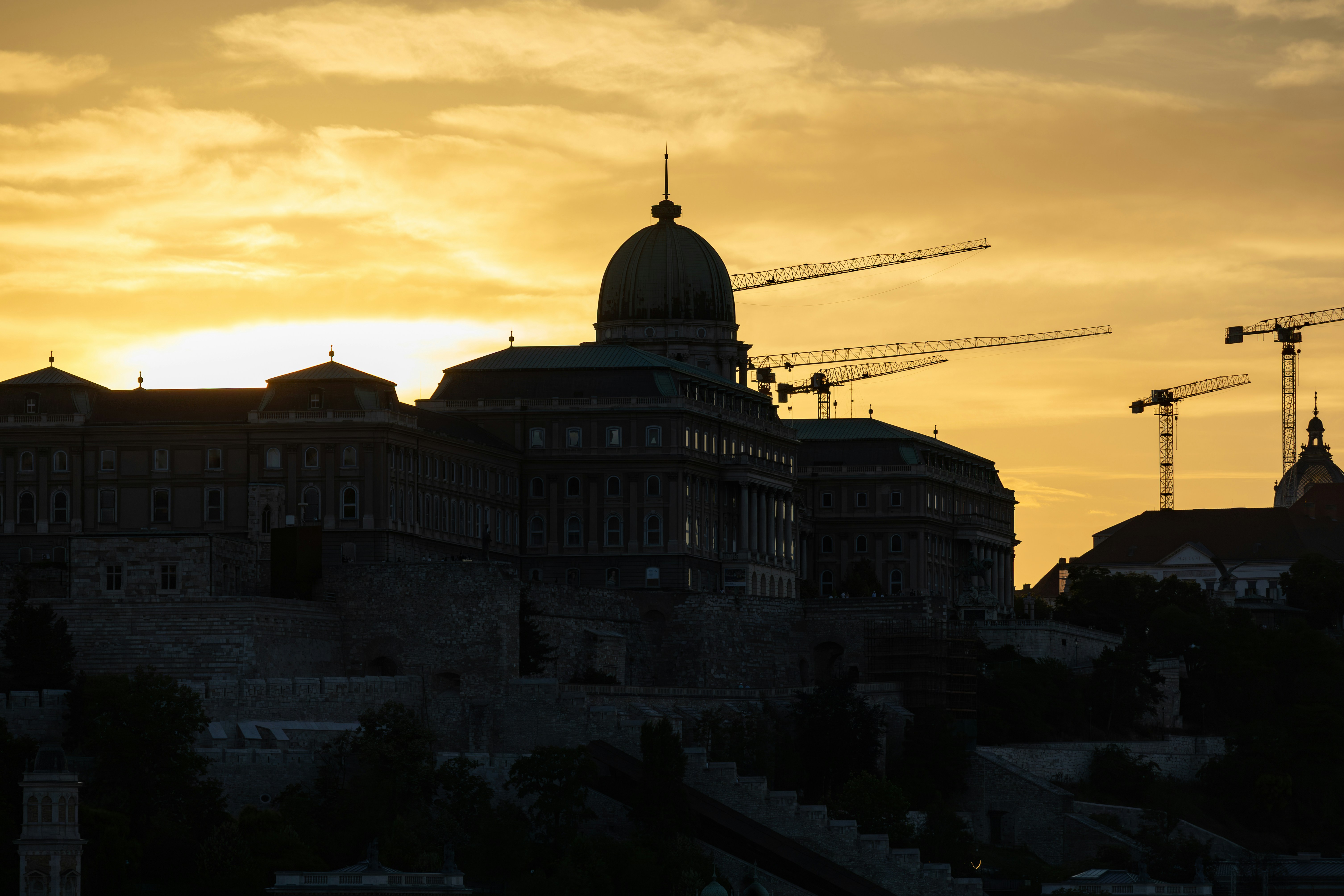 Building and cranes silhouetted against a golden sunset.