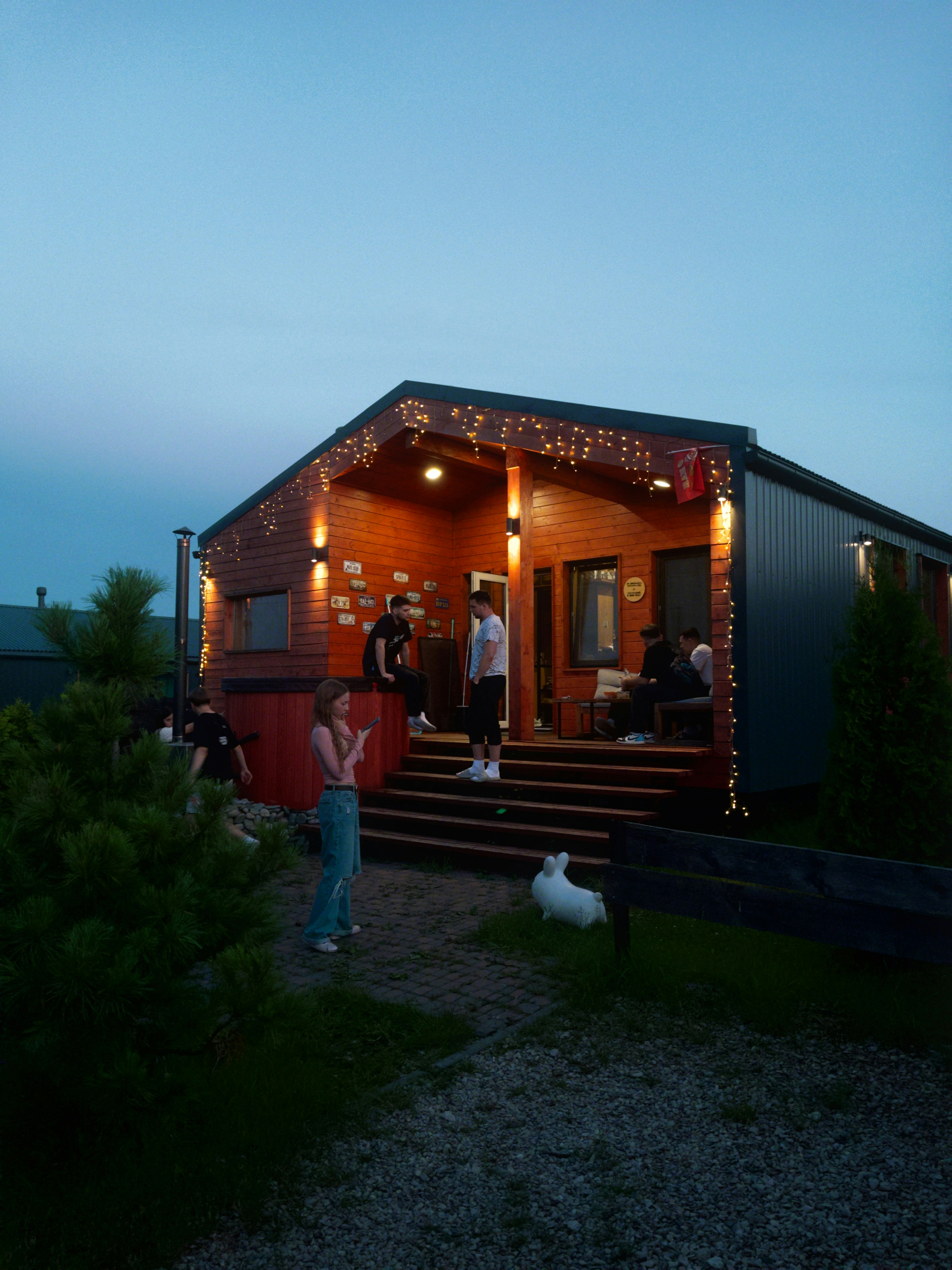 House decorated with lights, people on porch at dusk.