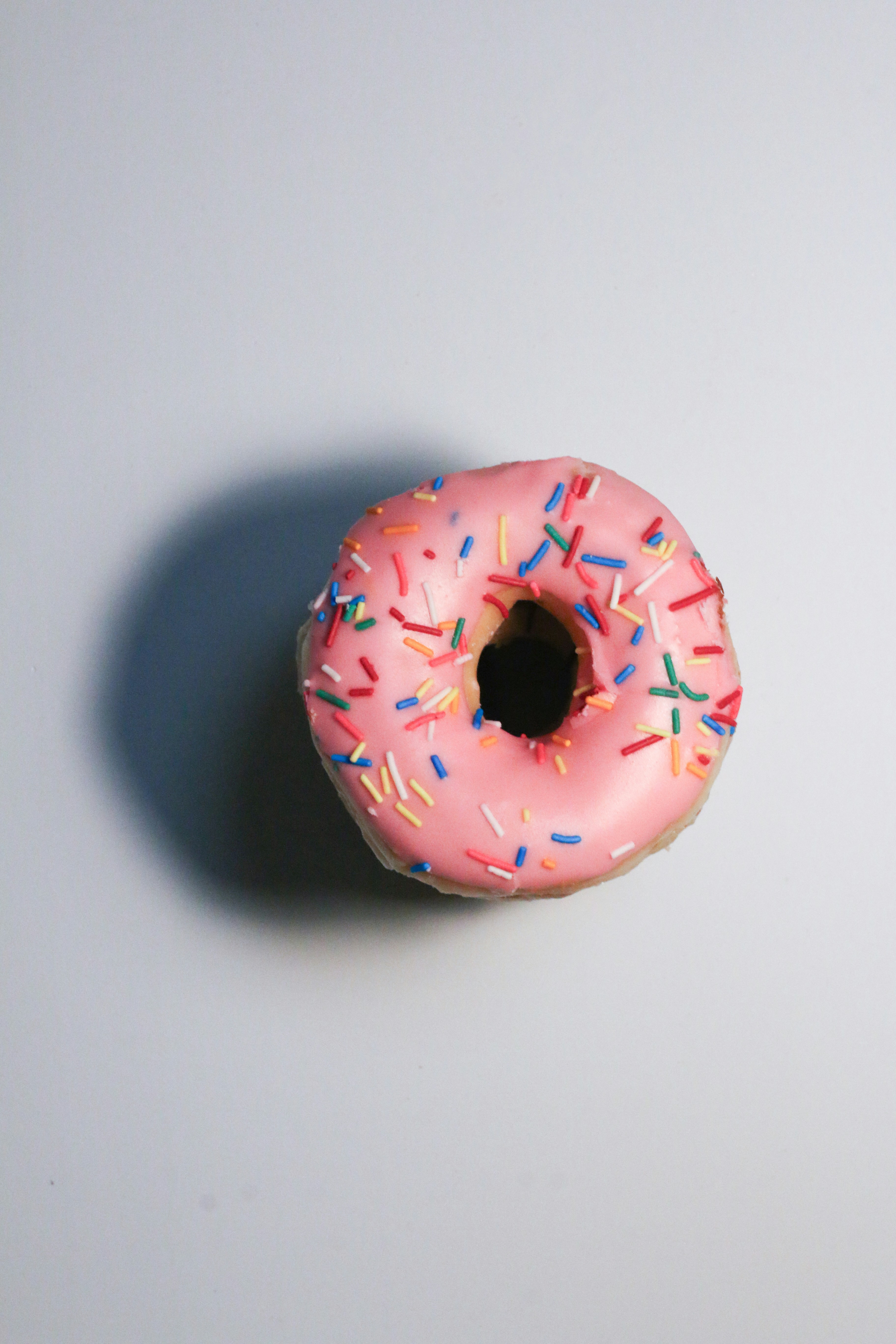 A pink donut with colorful sprinkles on a light background